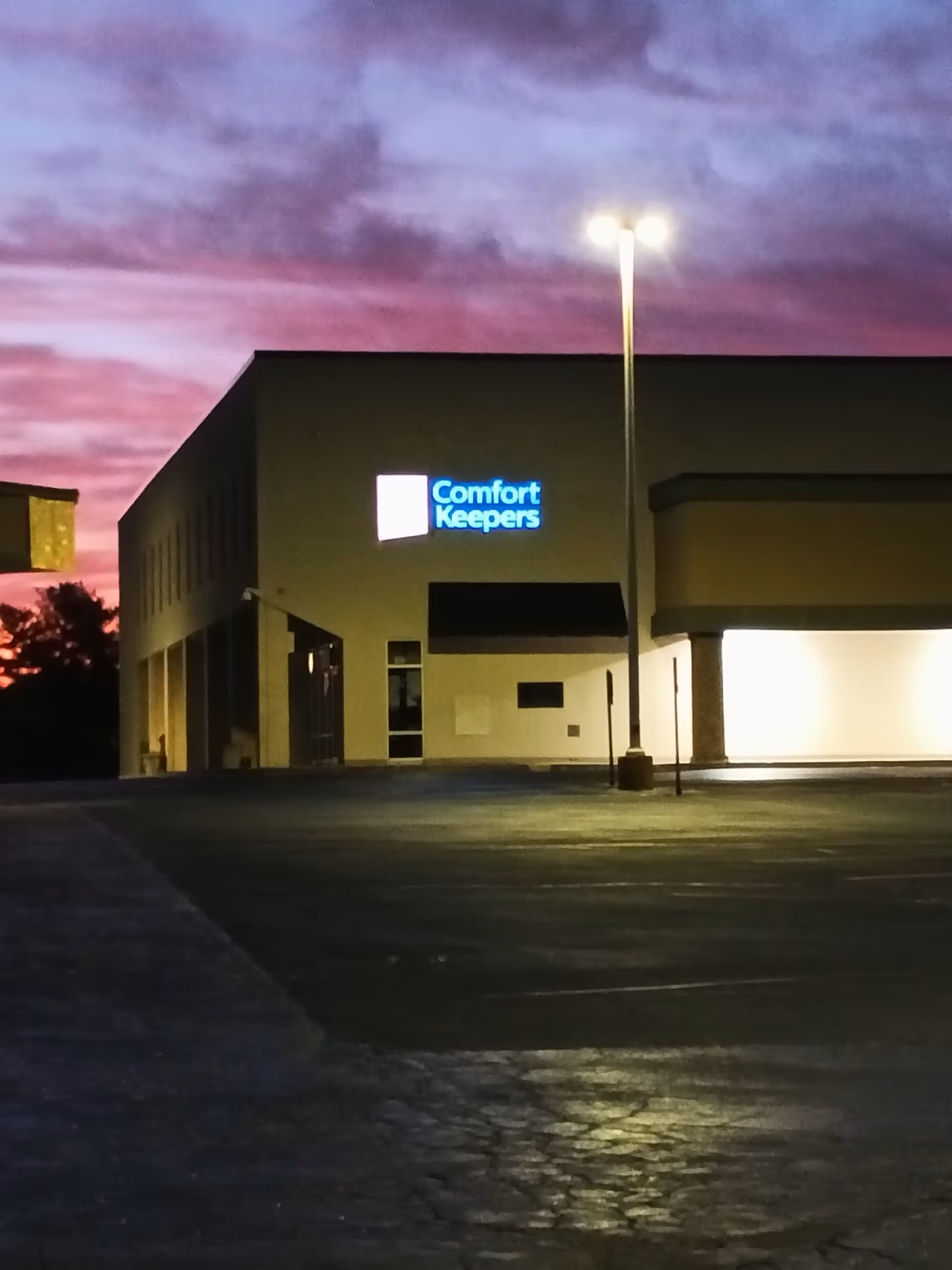 Exterior view of a Comfort Keepers building at dusk with a lit sign.