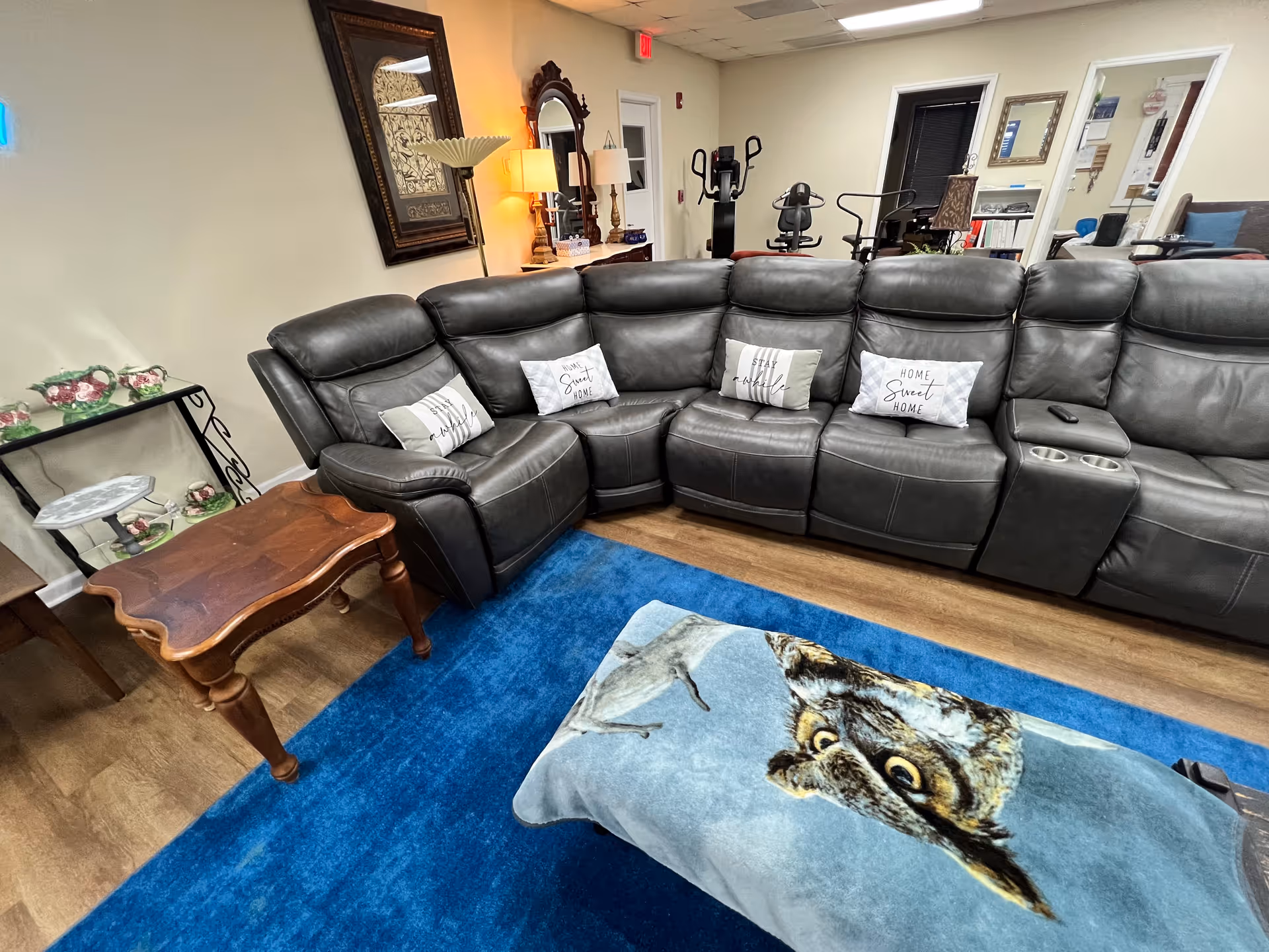 A spacious living room with a black leather sectional, blue rug, and decorative pillows.