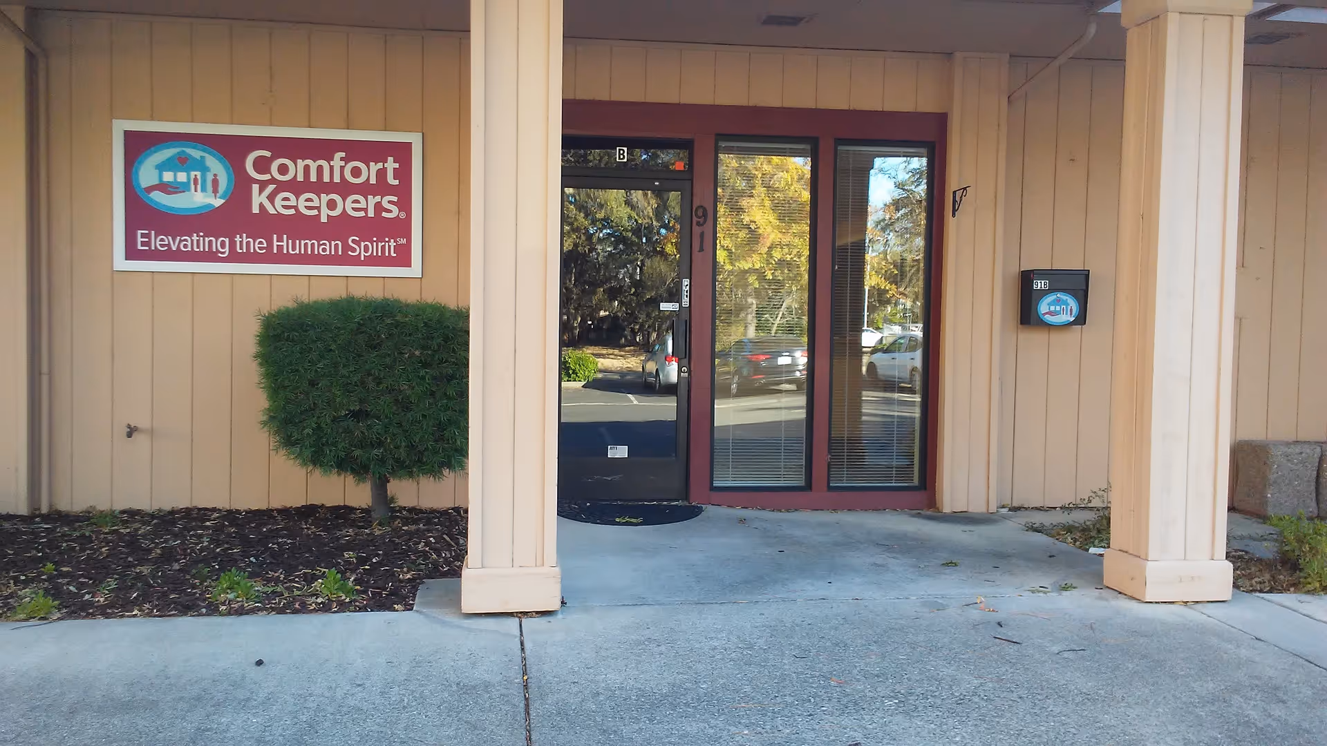Front entrance of Comfort Keepers Home Care with beige siding and glass doors.