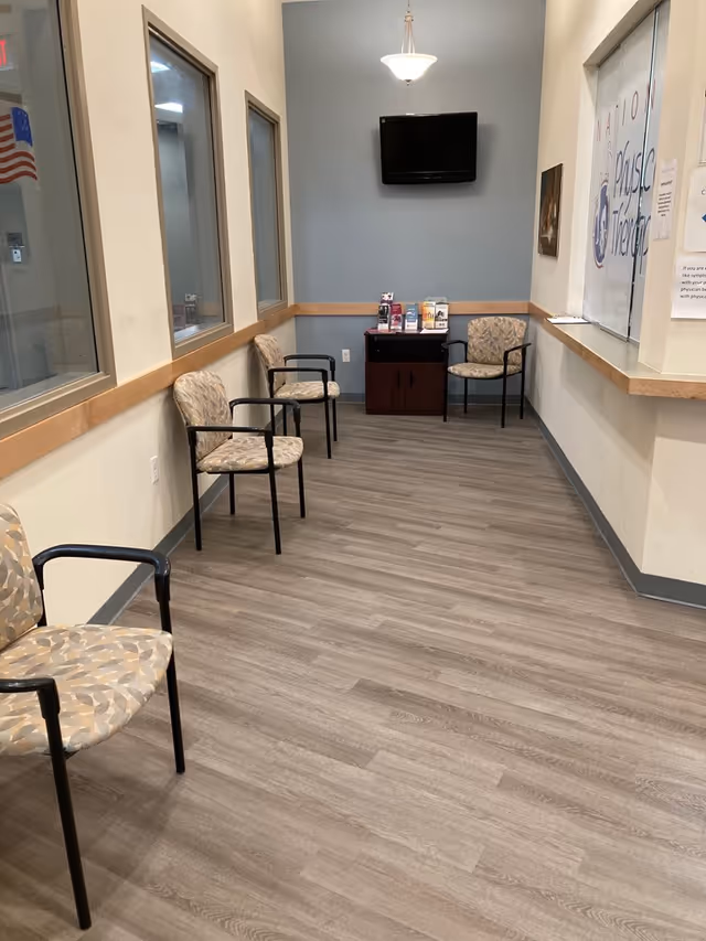 A waiting area inside a facility with chairs, a wall-mounted TV, and brochures.