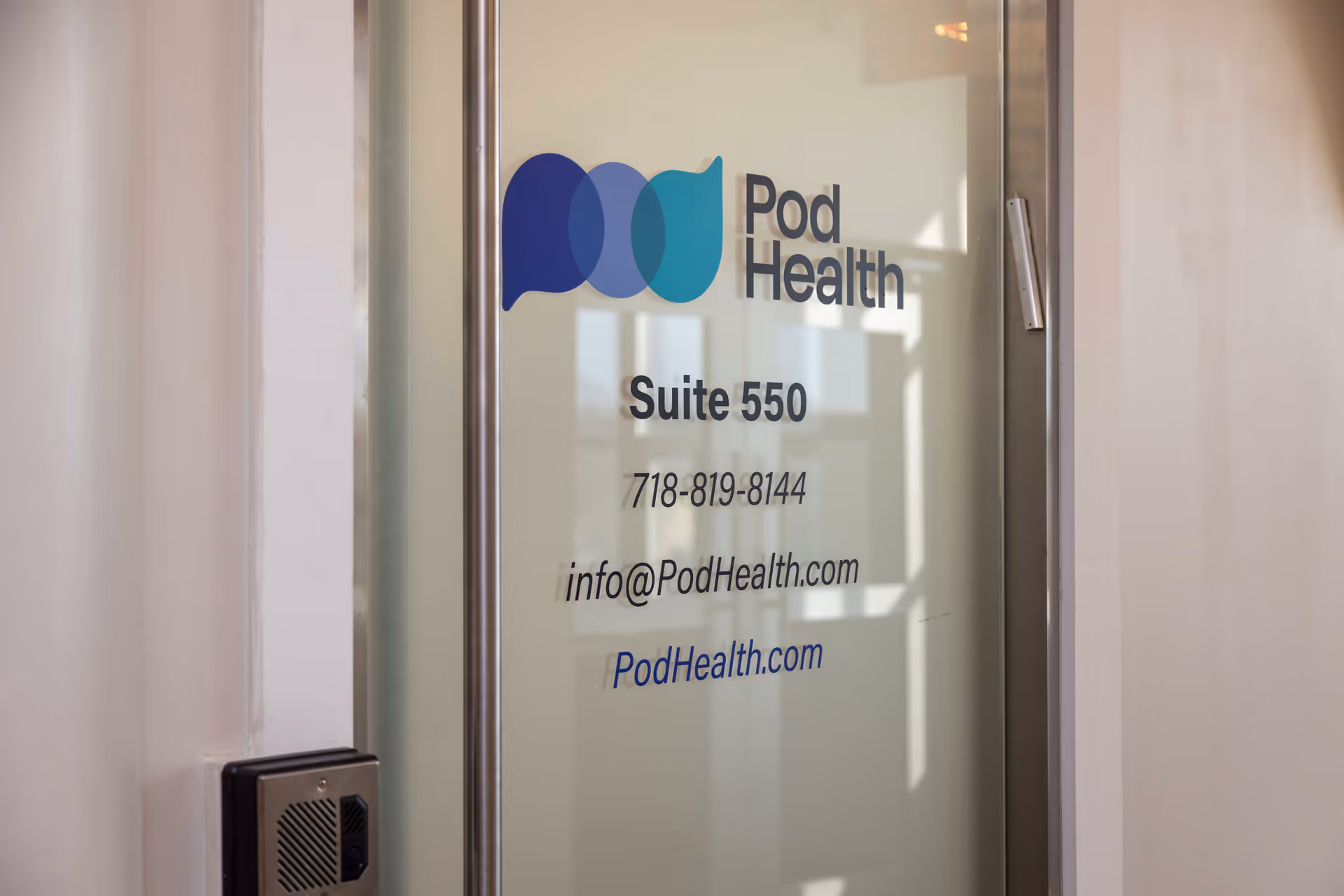 Glass door with Pod Health logo and Suite 550, displaying contact information inside a building.