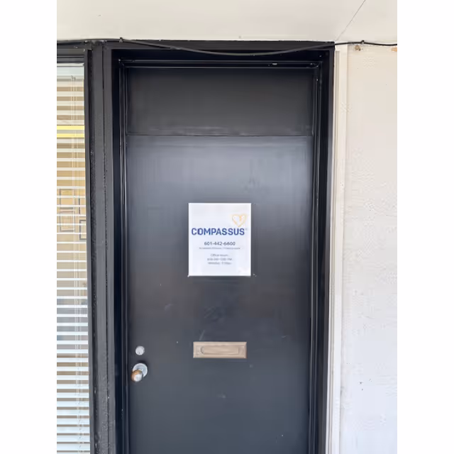 Dark exterior door with a Compassus sign posted in the middle.