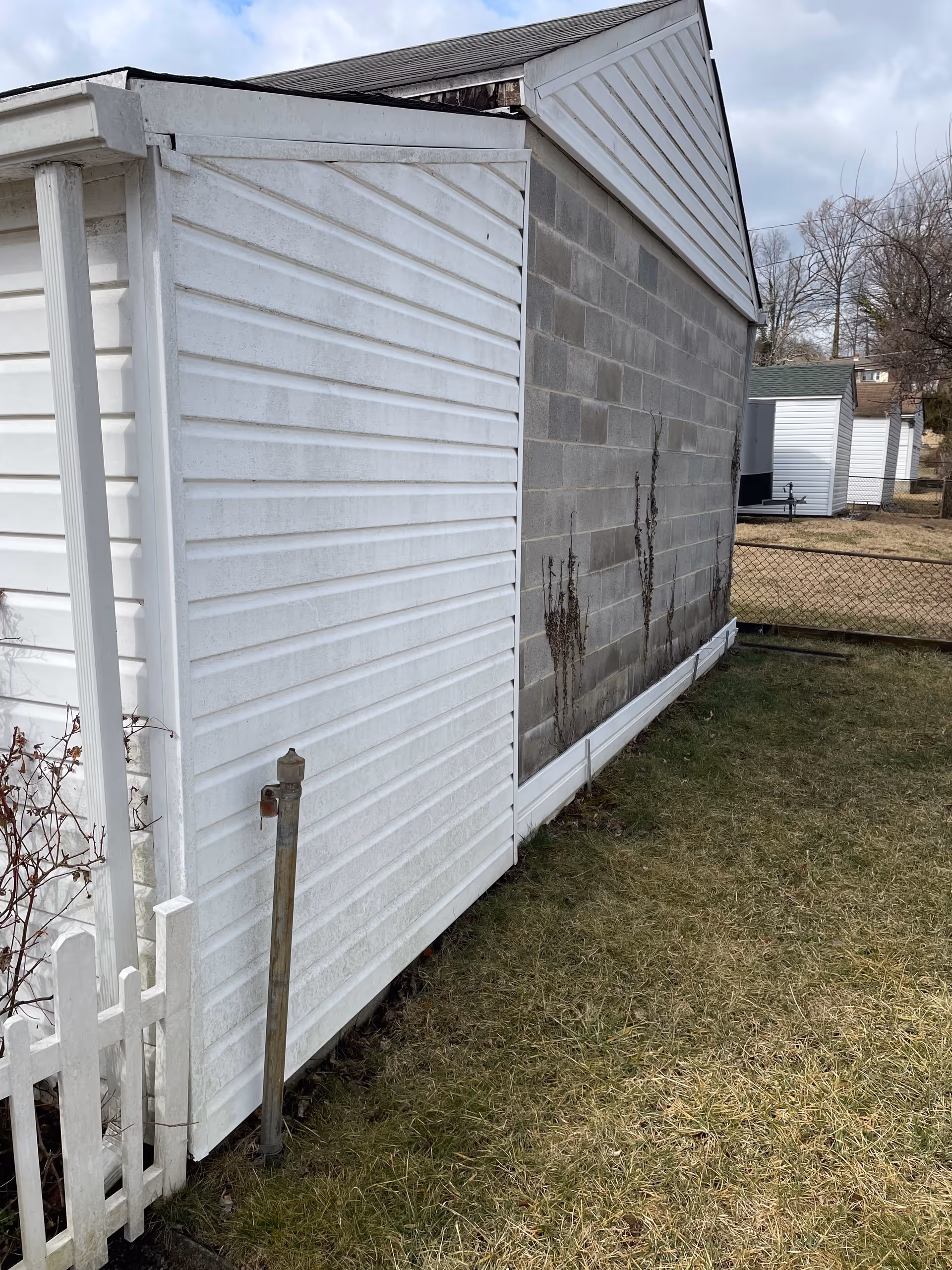 Exterior view of a white shedlike building with a block wall and small fence.