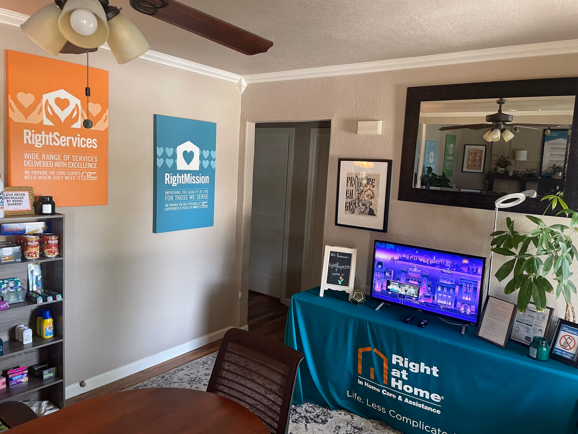 Reception area with branded Right at Home setup, monitor, posters, and a plant in cozy lobby.