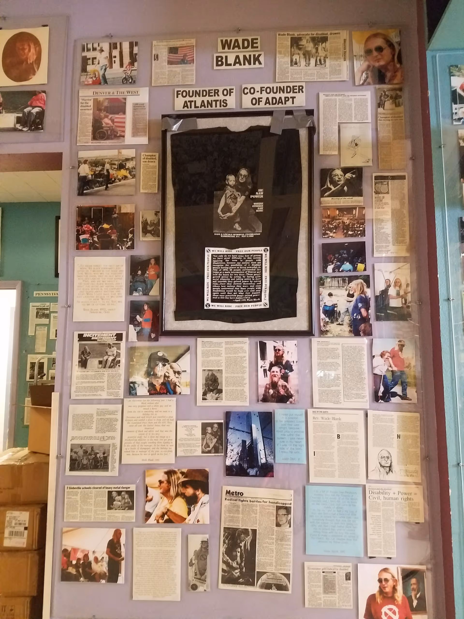 Purple wall covered with newspaper clippings and a central framed black display.