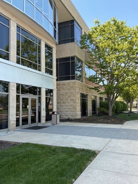 Modern two-story facility exterior with glass entrance doors and surrounding trees.
