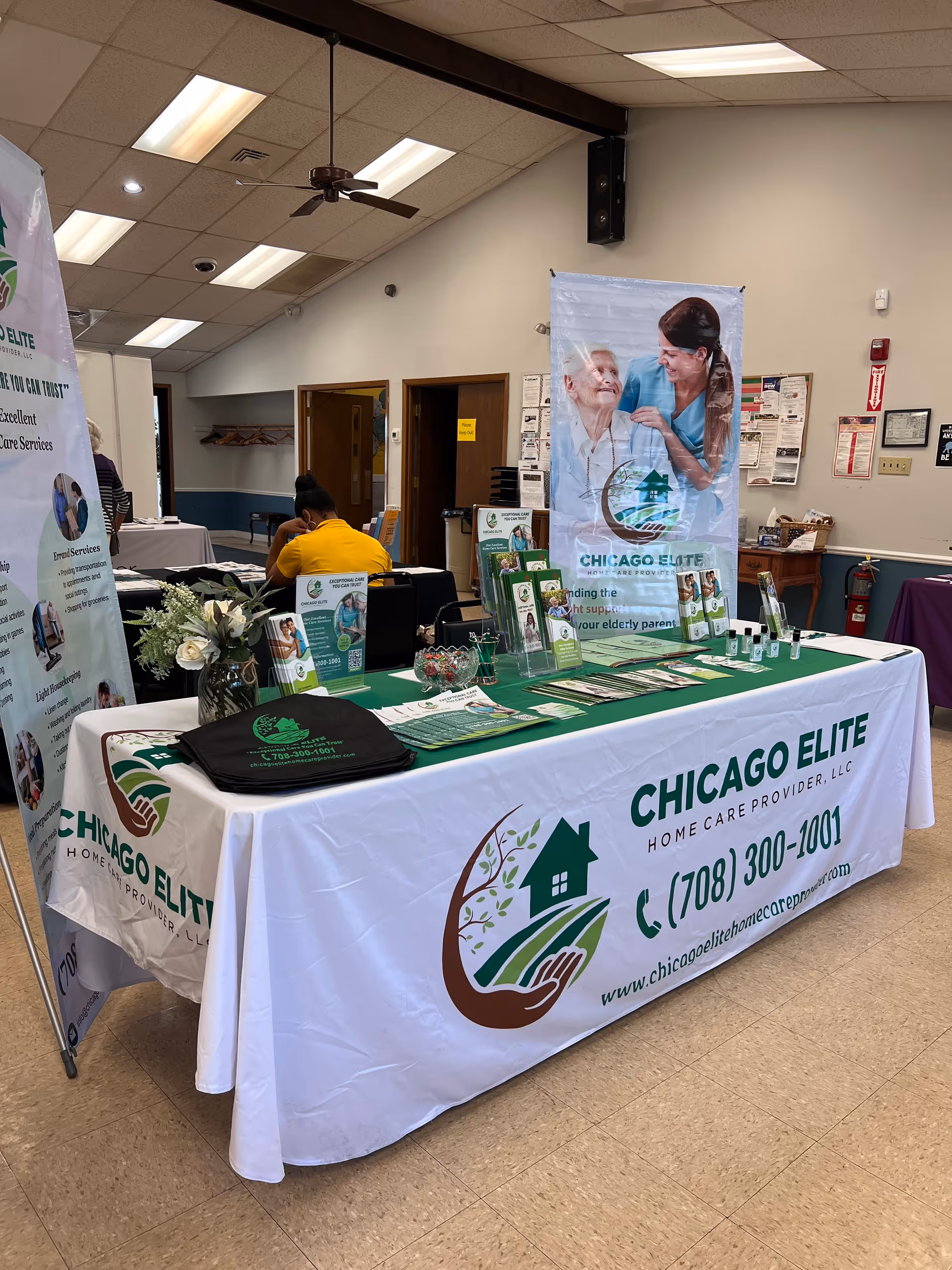 Promotional display table and banners for Chicago Elite Home Care in an indoor facility.