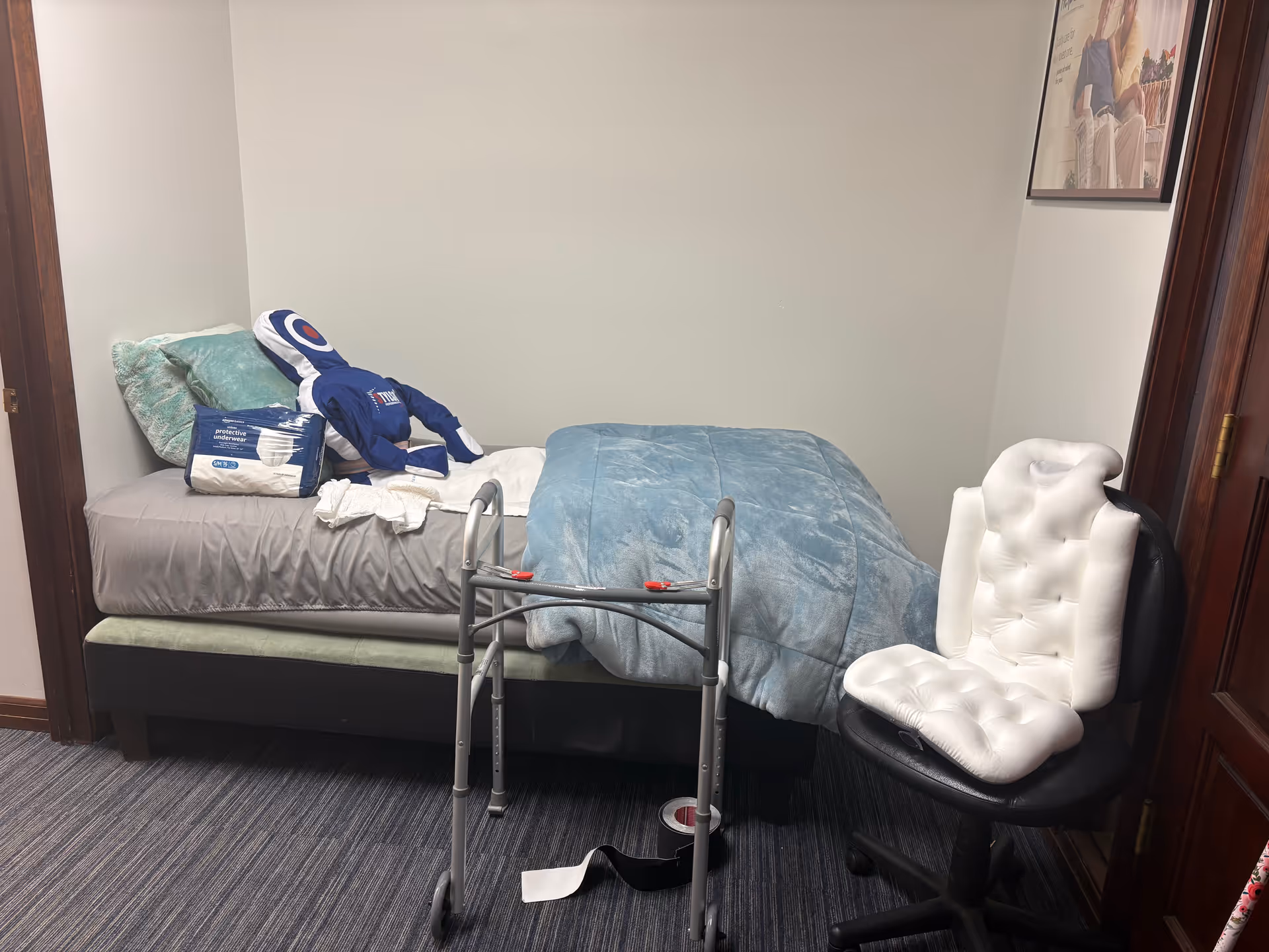 Small bedroom in a senior facility with a bed, walker, and cushioned chair.