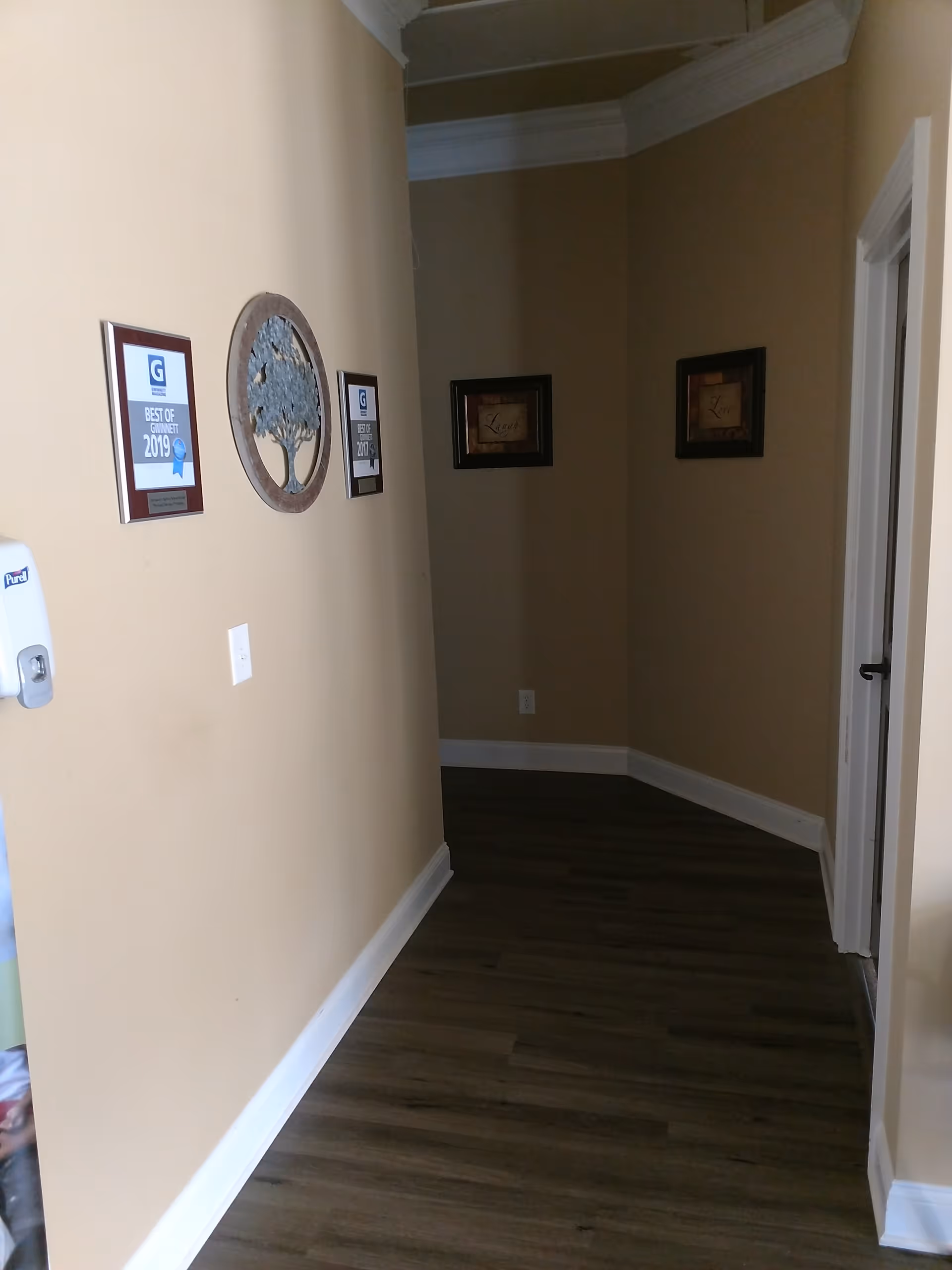 This beige interior hallway features wall plaques, art, and wood-look flooring.