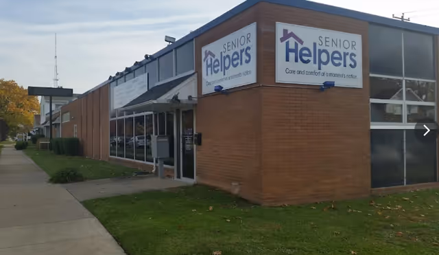 Exterior view of a Senior Helpers building with brick walls, signs, a sidewalk, and lawn.