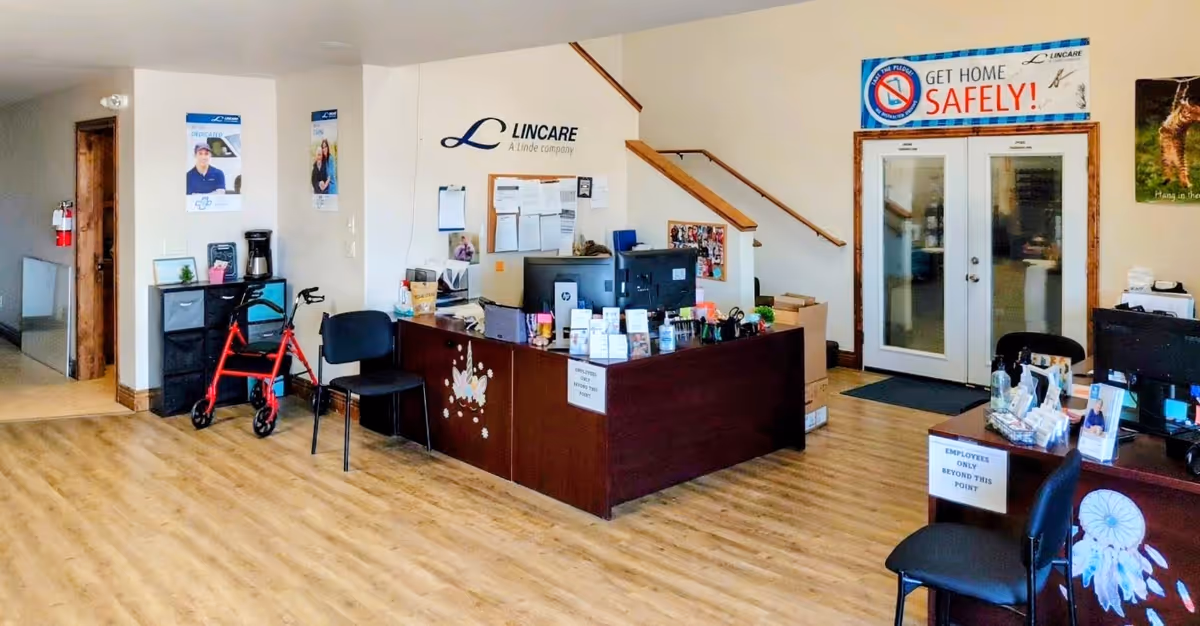 Reception area with a dark desk, chairs, walker, stairs, and signage in a LinCare lobby