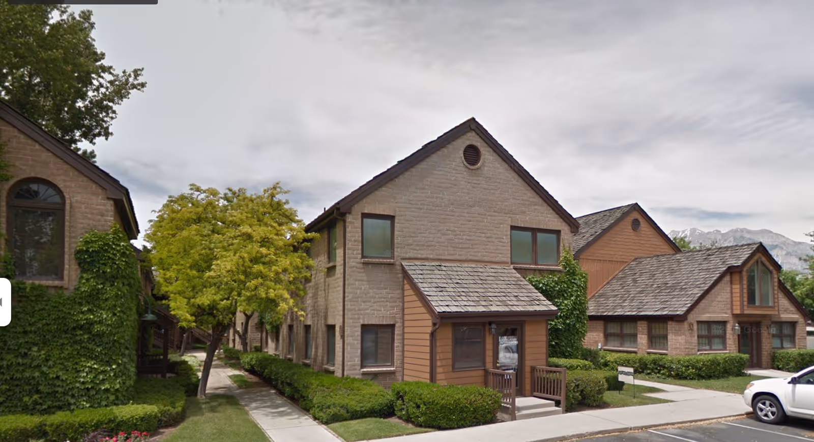 Exterior view of brick senior living homes with trees and manicured hedges.