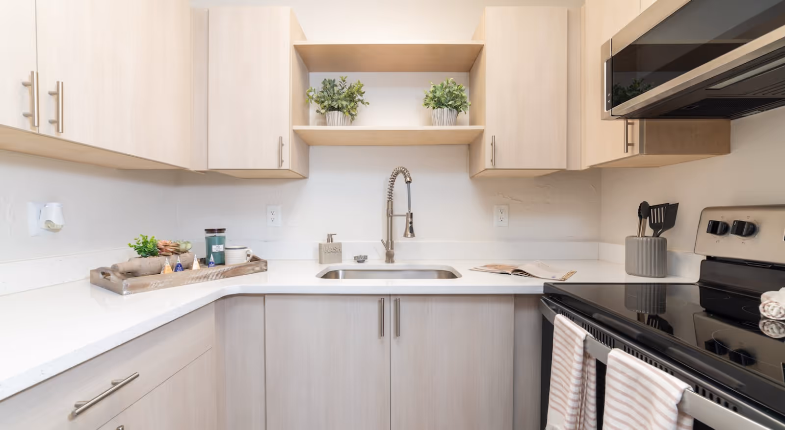 A modern kitchen with light wood cabinets, a central sink, and stainless steel appliances.