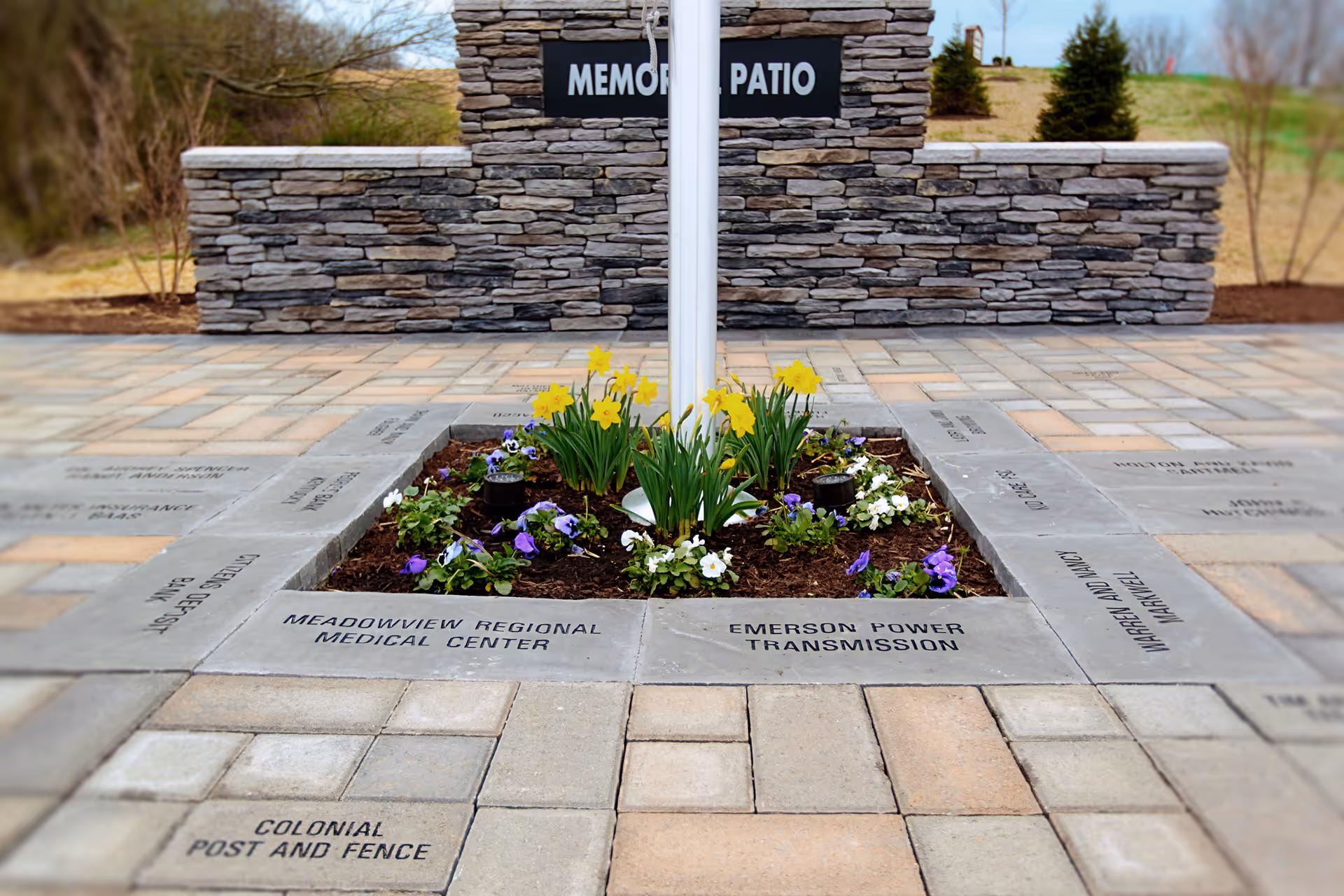Outdoor memorial patio featuring a central flower bed surrounded by engraved concrete tiles.