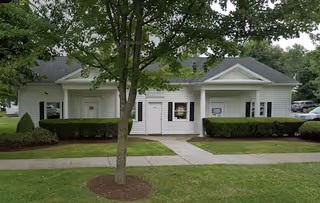 Exterior view of a single-story Comfort Keepers facility with a walkway and trees.
