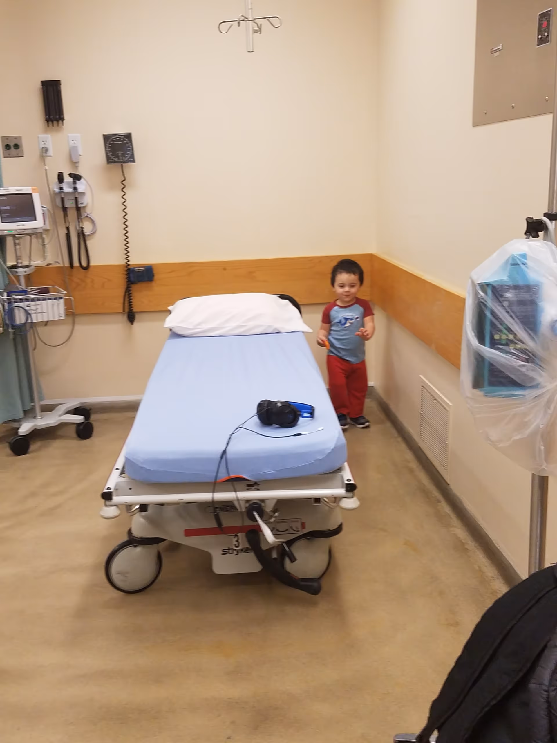 Hospital bed in a clinical room with medical equipment and a child nearby.