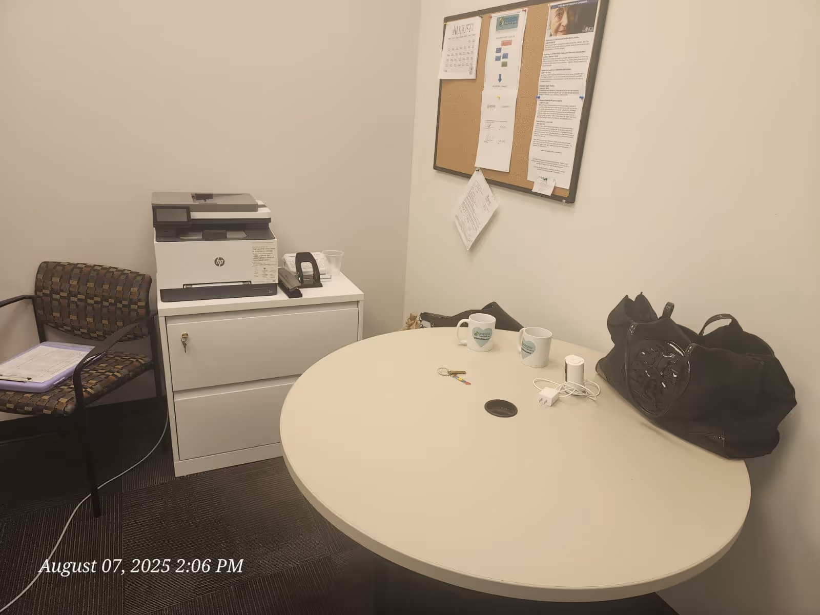 Small office area with round table, printer, corkboard, chair, and a handbag in a senior facility.