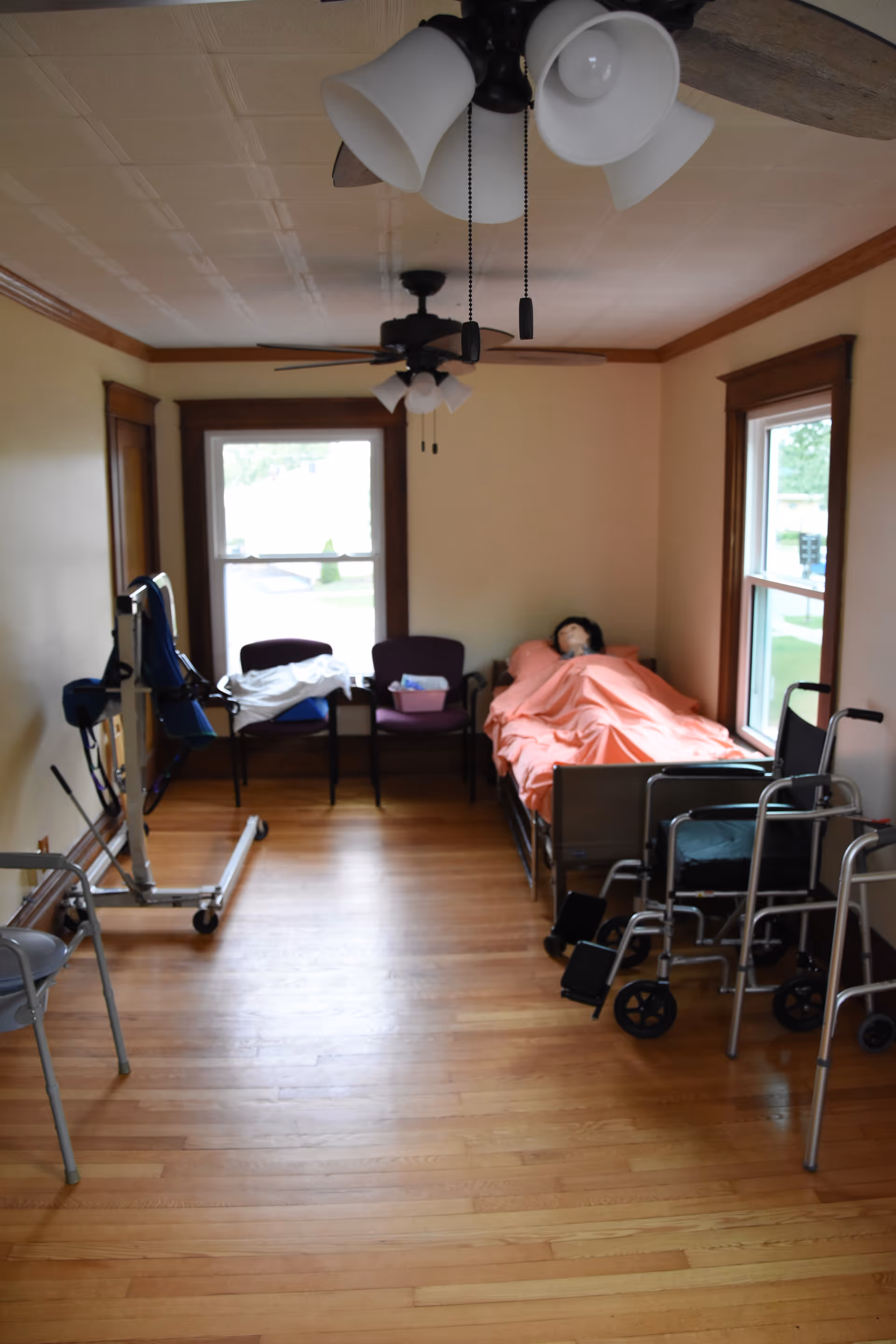 Assisted living bedroom in a Right at Home facility with bed, chairs, walker, and wheelchair.
