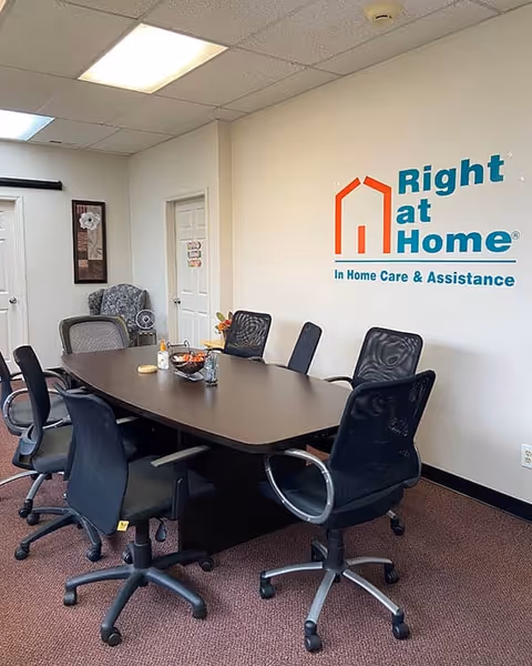 A conference room with a dark table, office chairs, and Right at Home logo on wall.