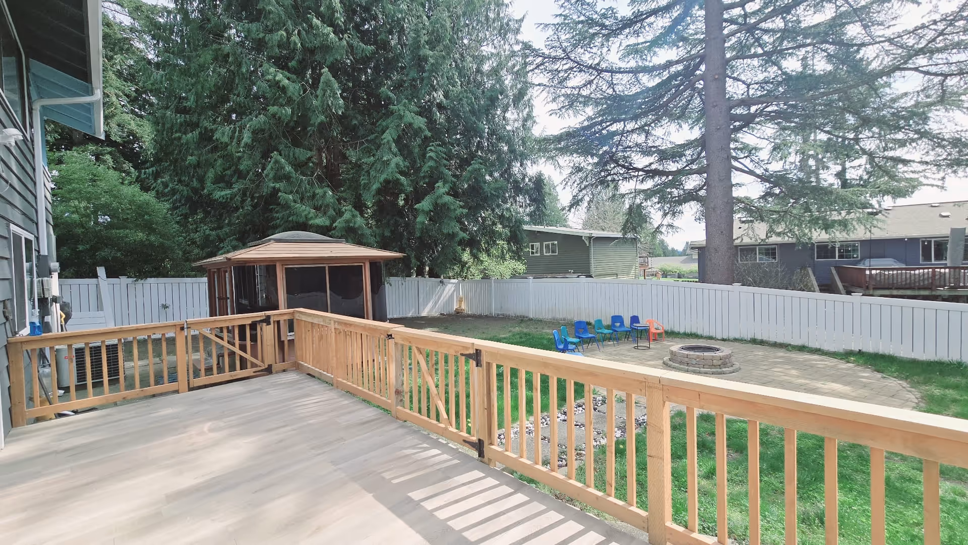 Wooden deck overlooking a fenced backyard with a fire pit and blue chairs.