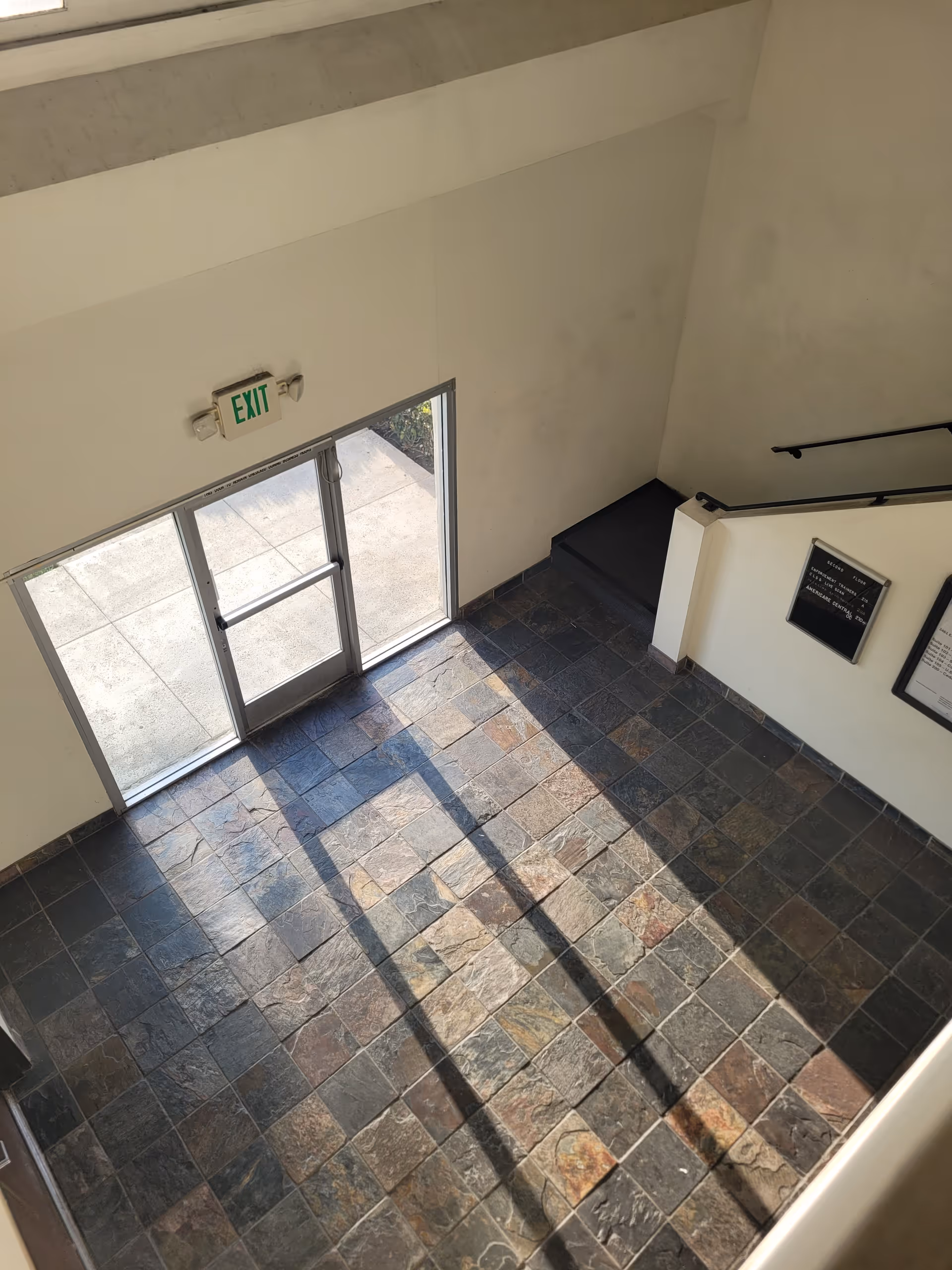 Tiled interior lobby with glass doors, an exit sign, and a staircase.