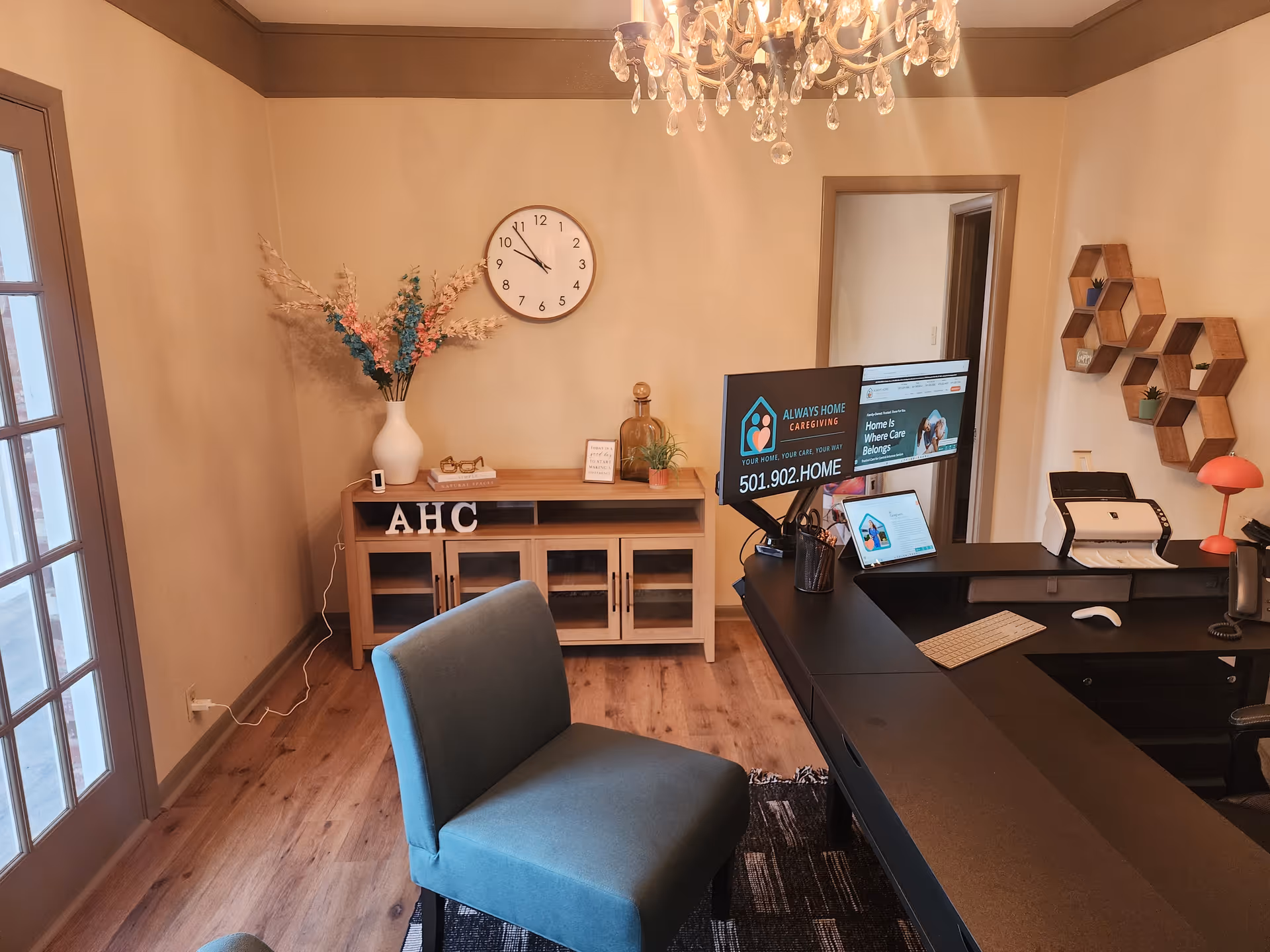 Reception area with desk, chandelier, wall clock, blue chair, and AHC decor.