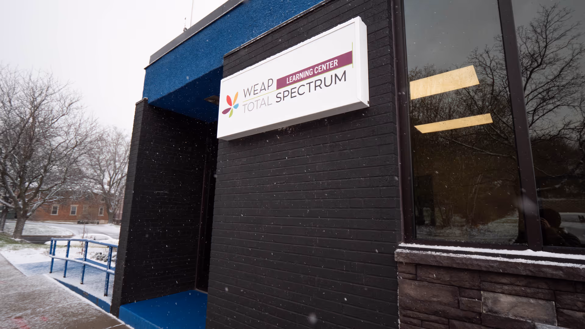 Exterior of a dark brick building entrance with a WEAP Total Spectrum sign.