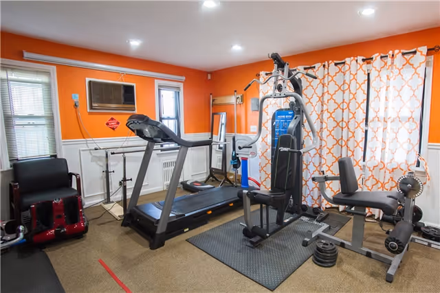 A compact fitness room with treadmill and weight machines against orange walls.