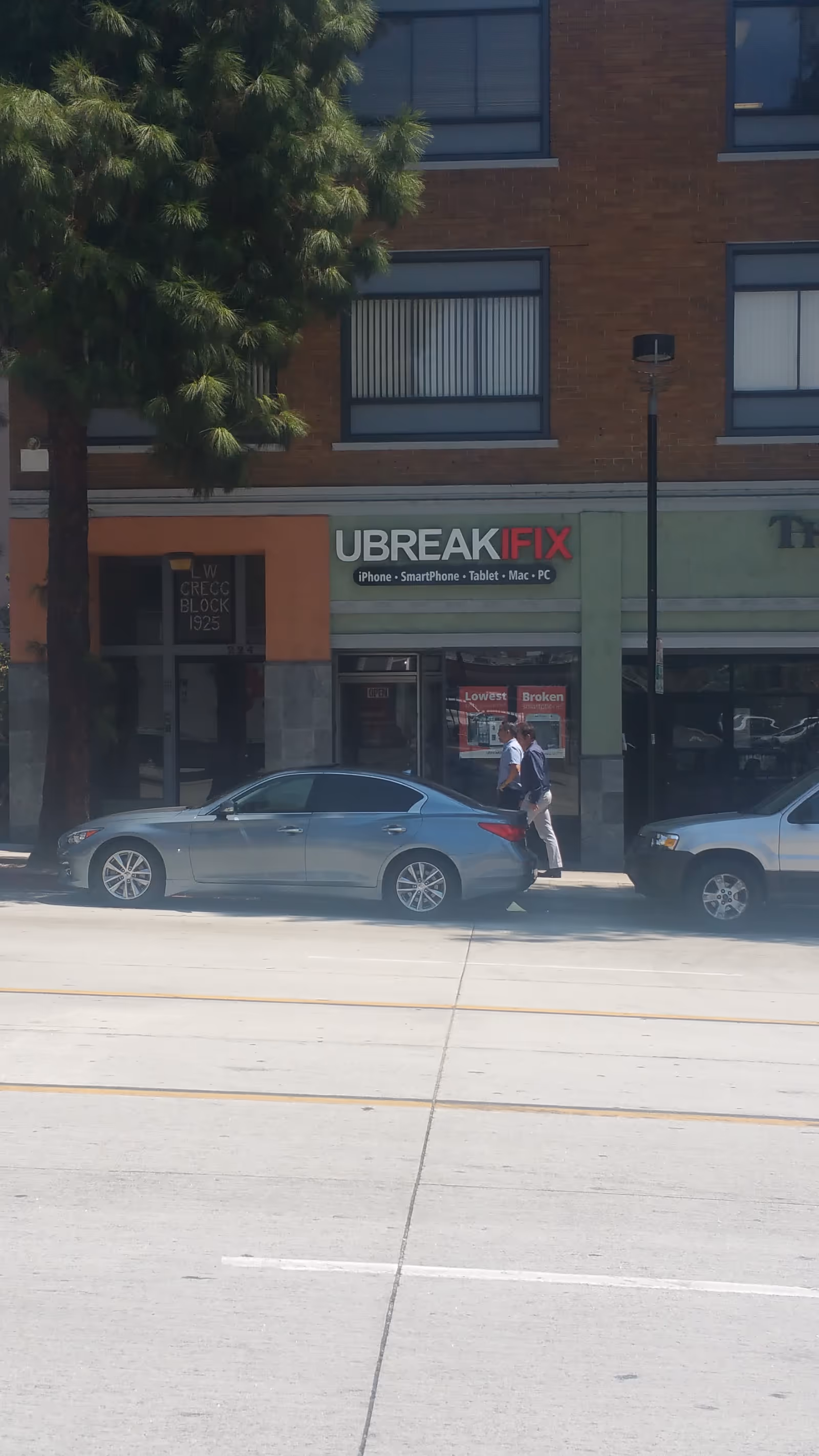 Street view of a brick building with UBREAKIFIX storefront, cars, and pedestrians.