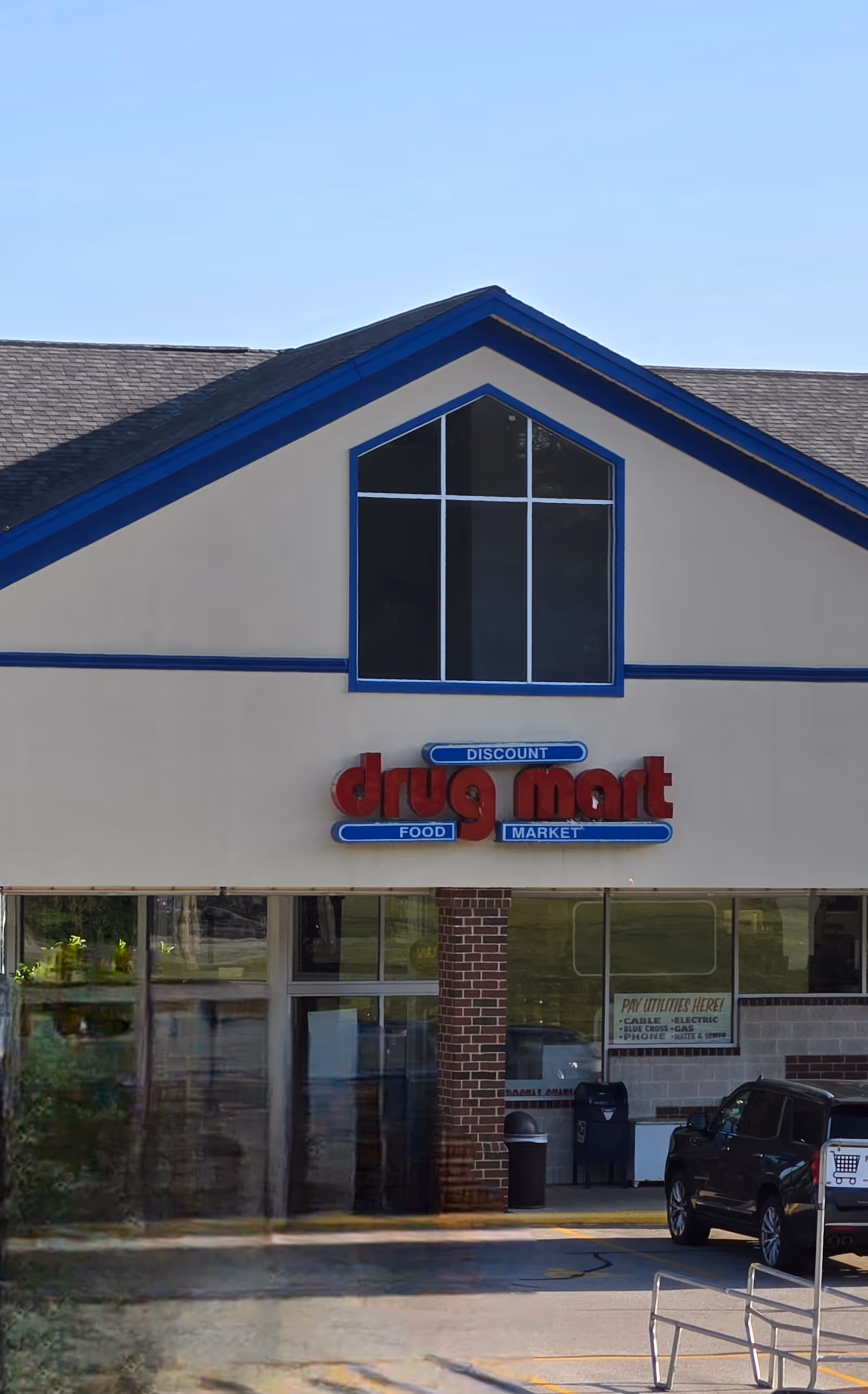 Front view of Discount Drug Mart storefront with triangular peaked window and parking