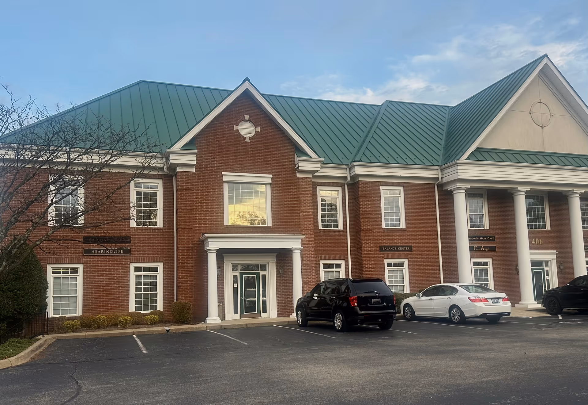 Exterior view of a brick senior living facility with green metal roof and columns.