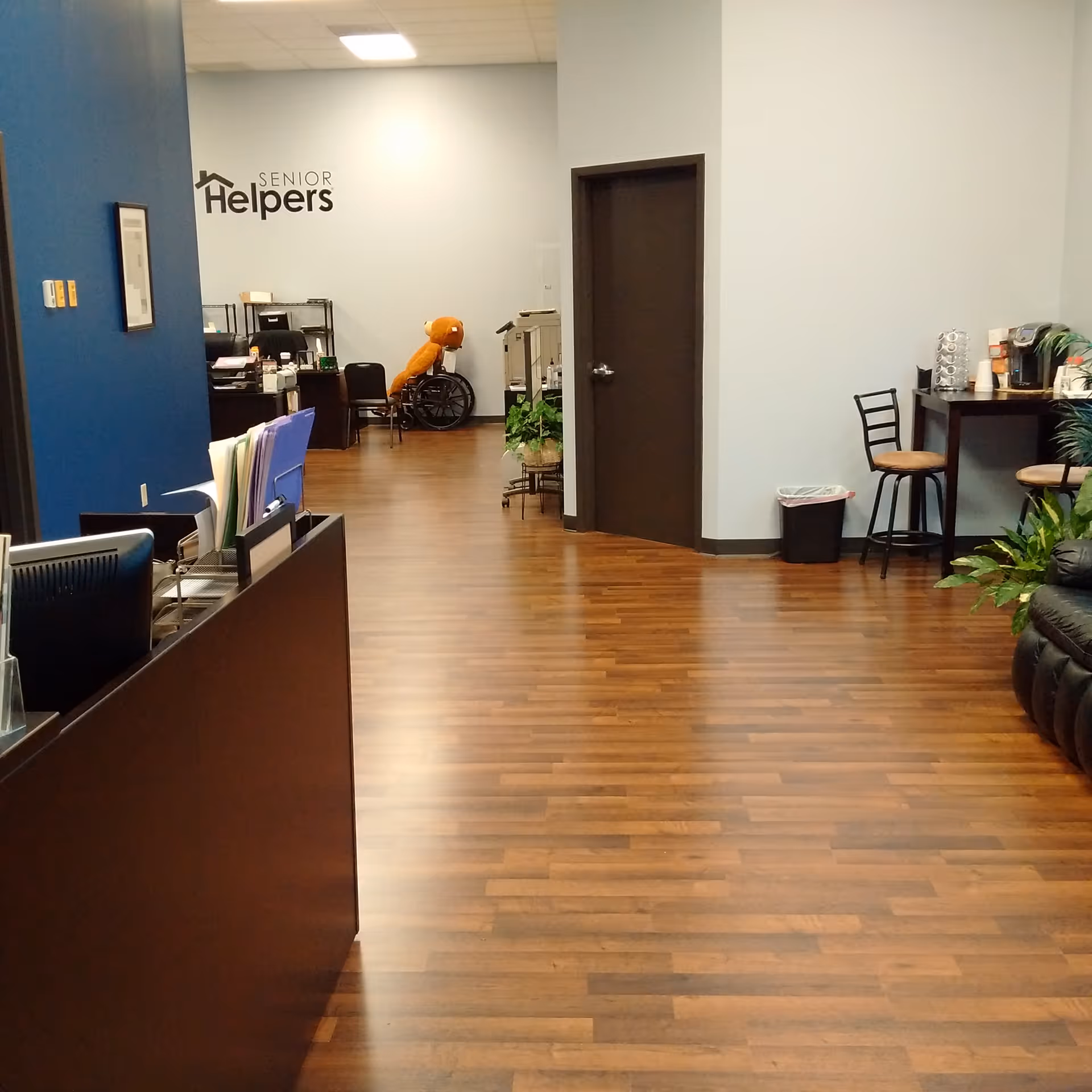 Reception area of Senior Helpers facility with blue wall, logo, and wooden floor.