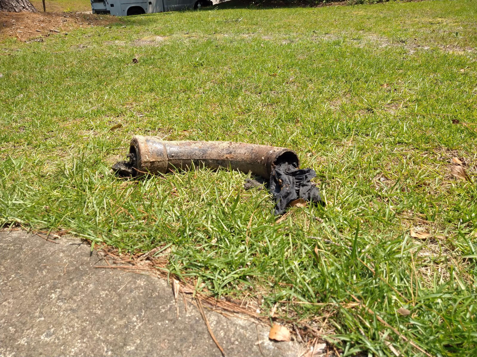 Rusted metal pipe on a grassy lawn with torn fabric nearby