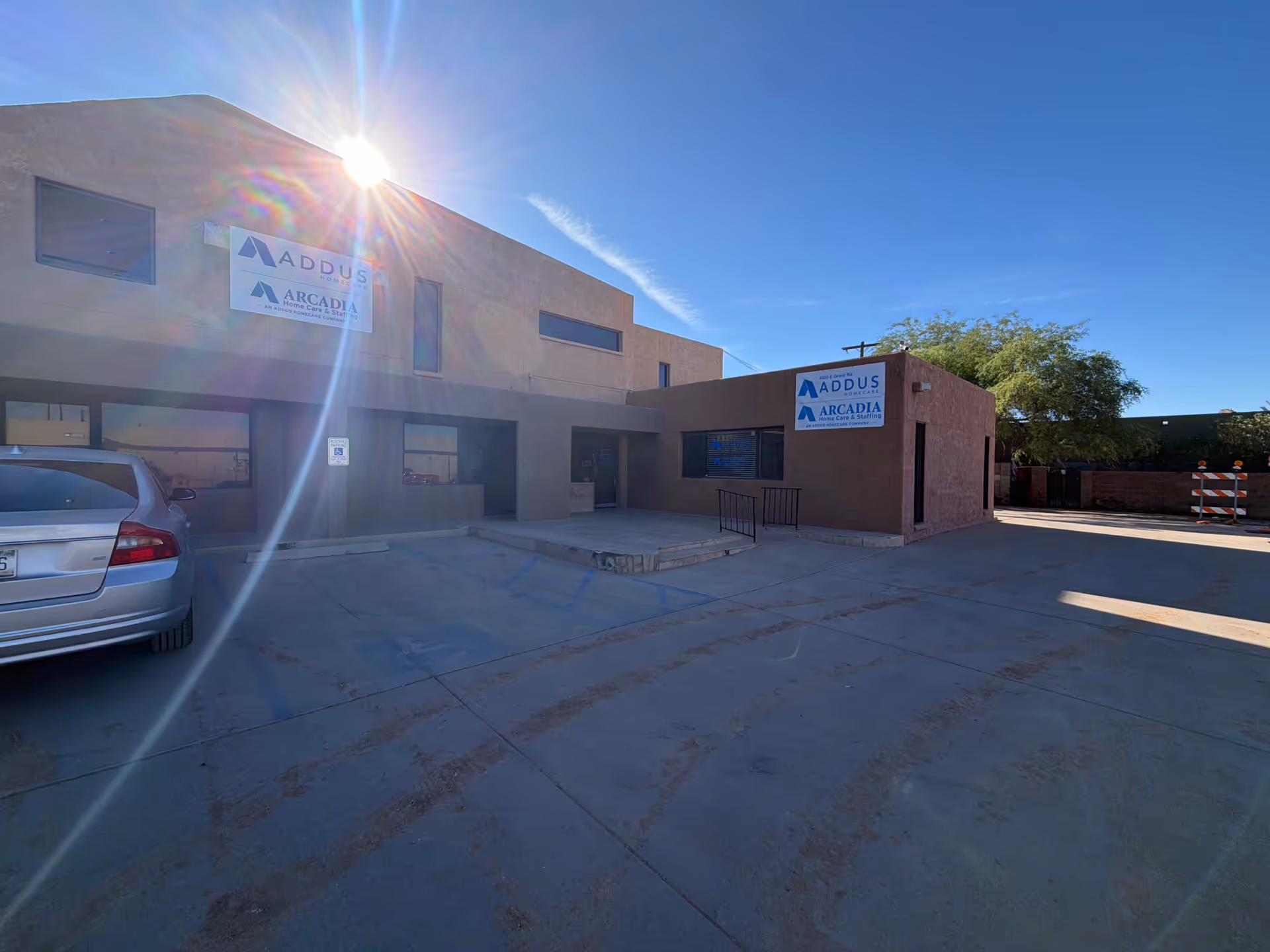 Sunlit exterior view of Arcadia Home Care & Staffing building with parked car.
