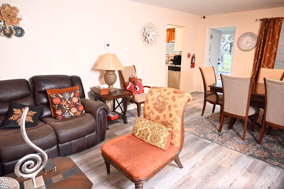 Cozy living room in a senior facility with leather sofa, armchair, and dining area.
