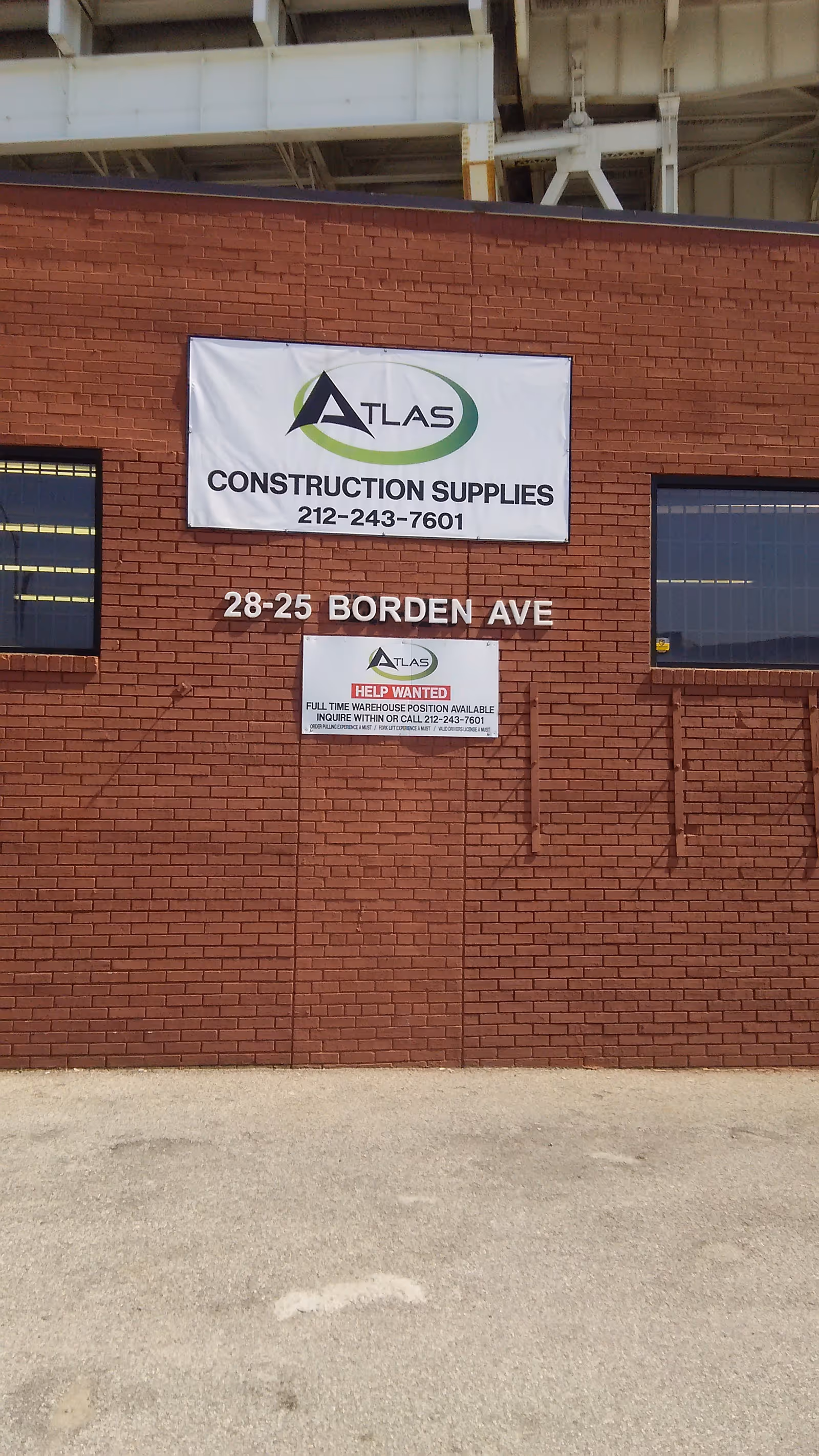 Brick building exterior with Atlas Construction Supplies banners and address 28-25 Borden Ave