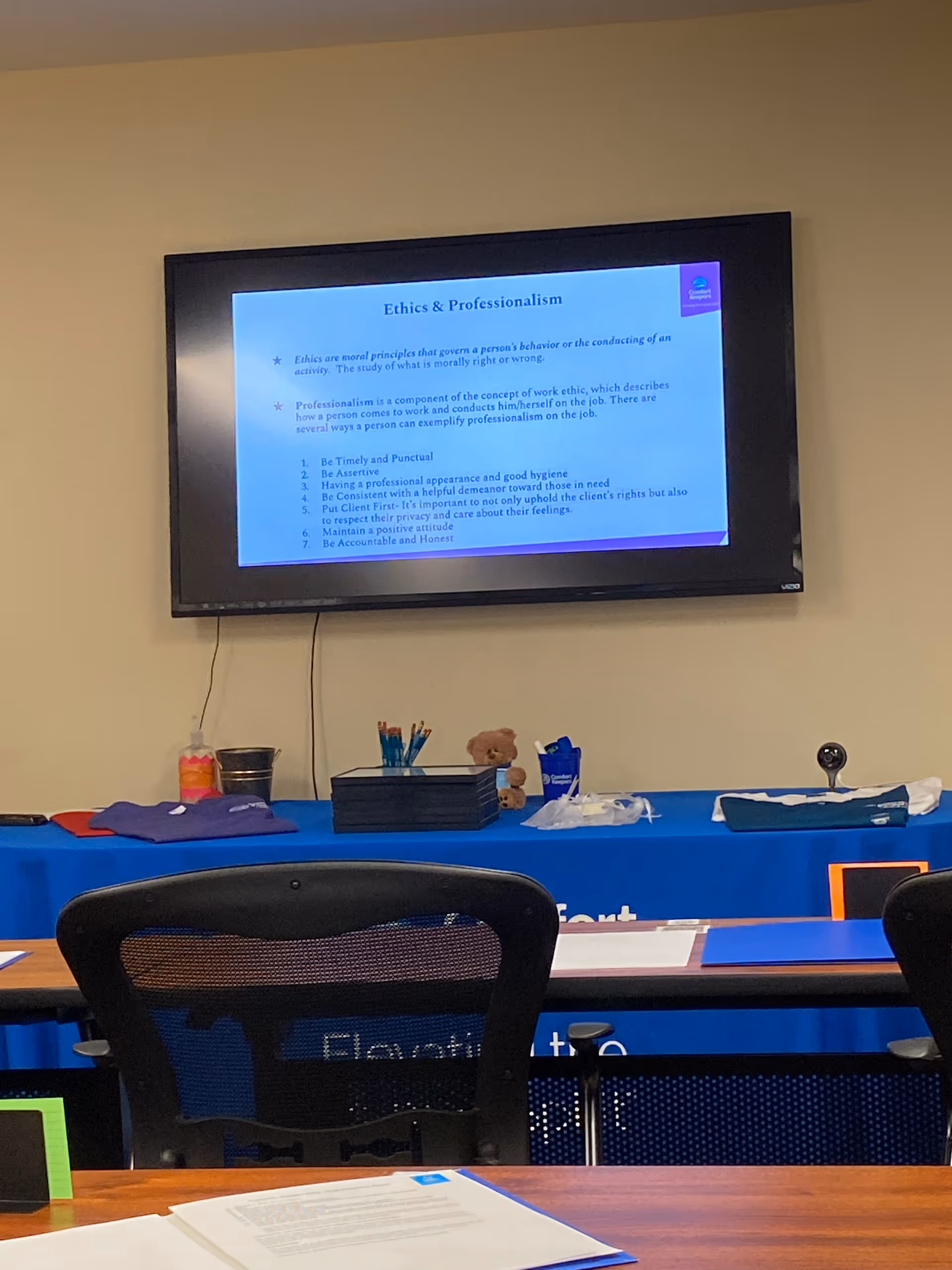 Interior conference room with a wall-mounted screen displaying Ethics and Professionalism over a blue-clothed table.