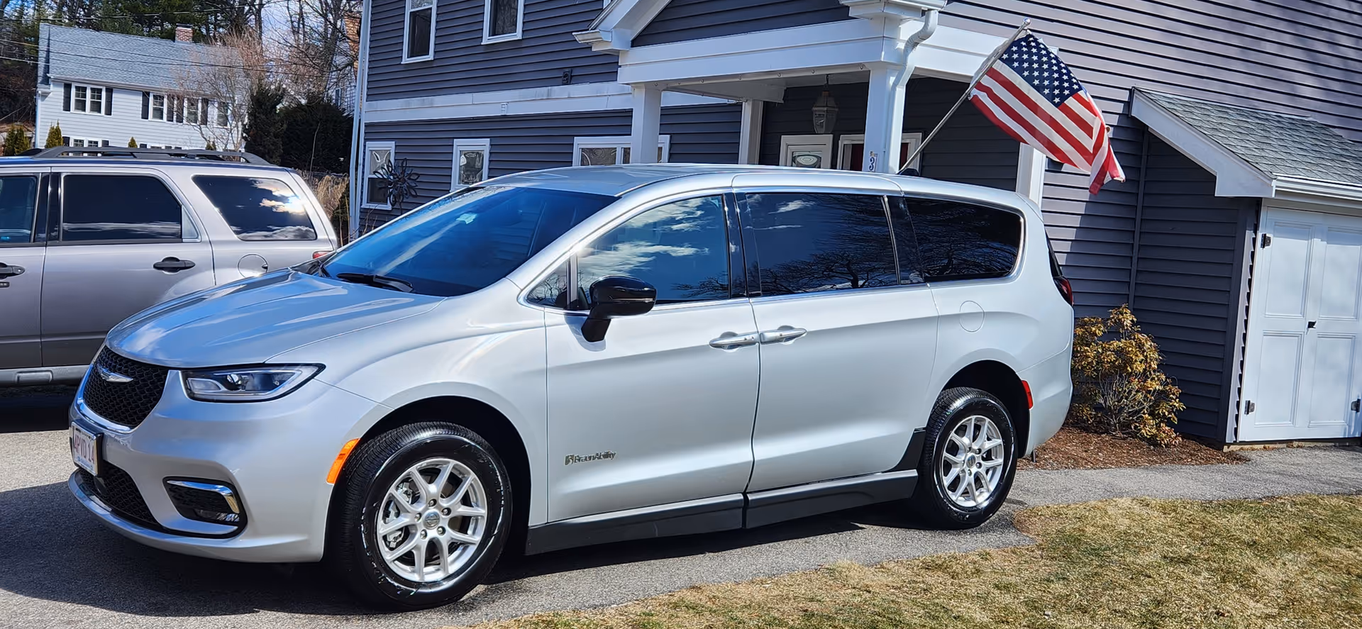 Silver minivan parked in a driveway in front of a blue house with an American flag
