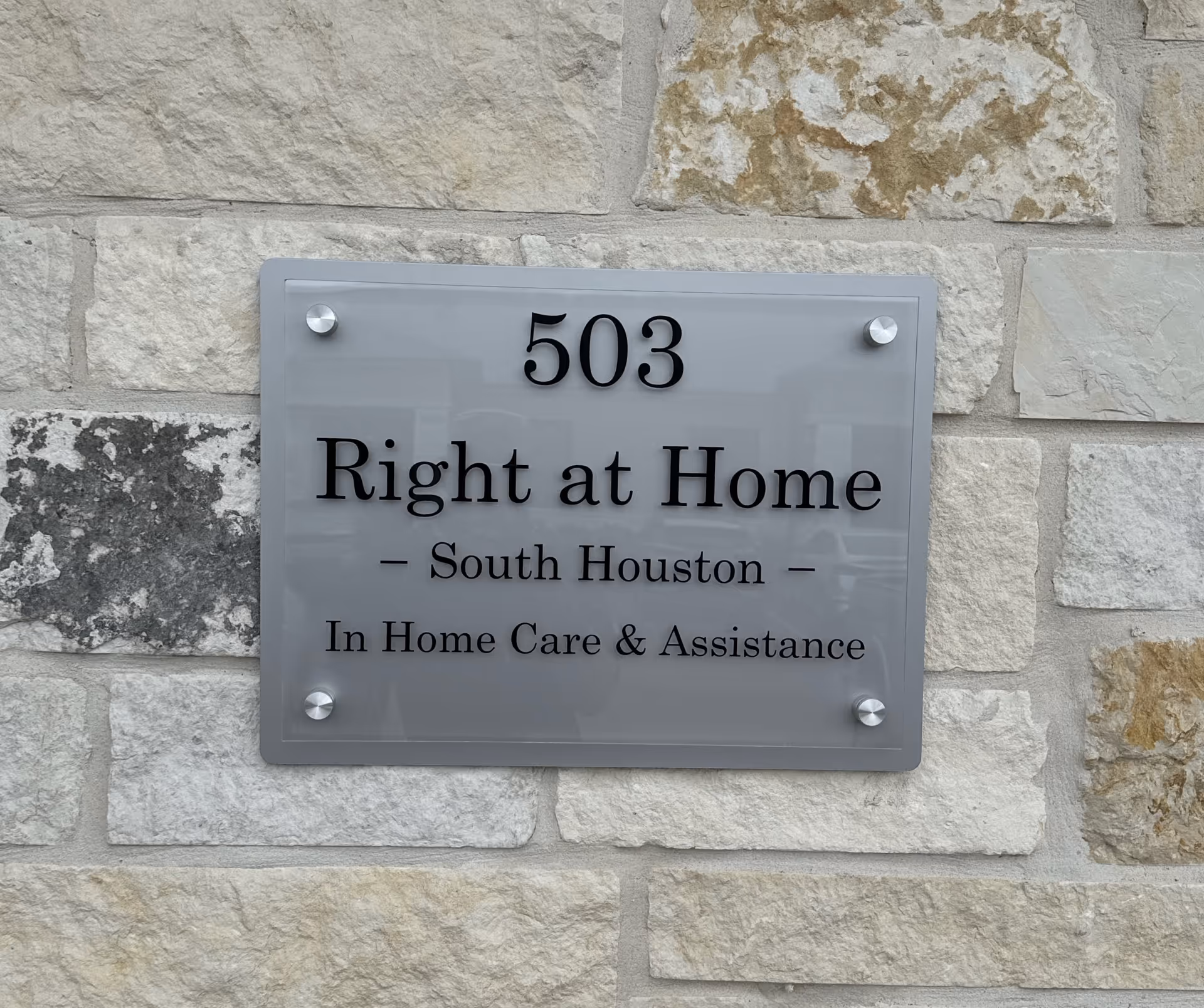 Gray metal sign on a stone wall displaying Right at Home and care details.
