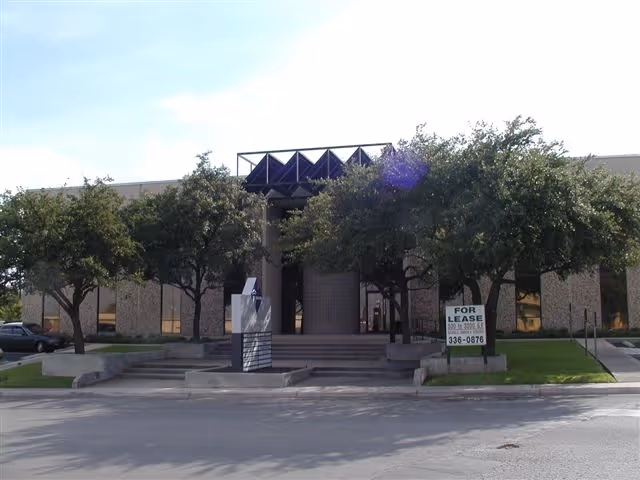 A modern building exterior with trees, steps, and a For Lease sign in front.