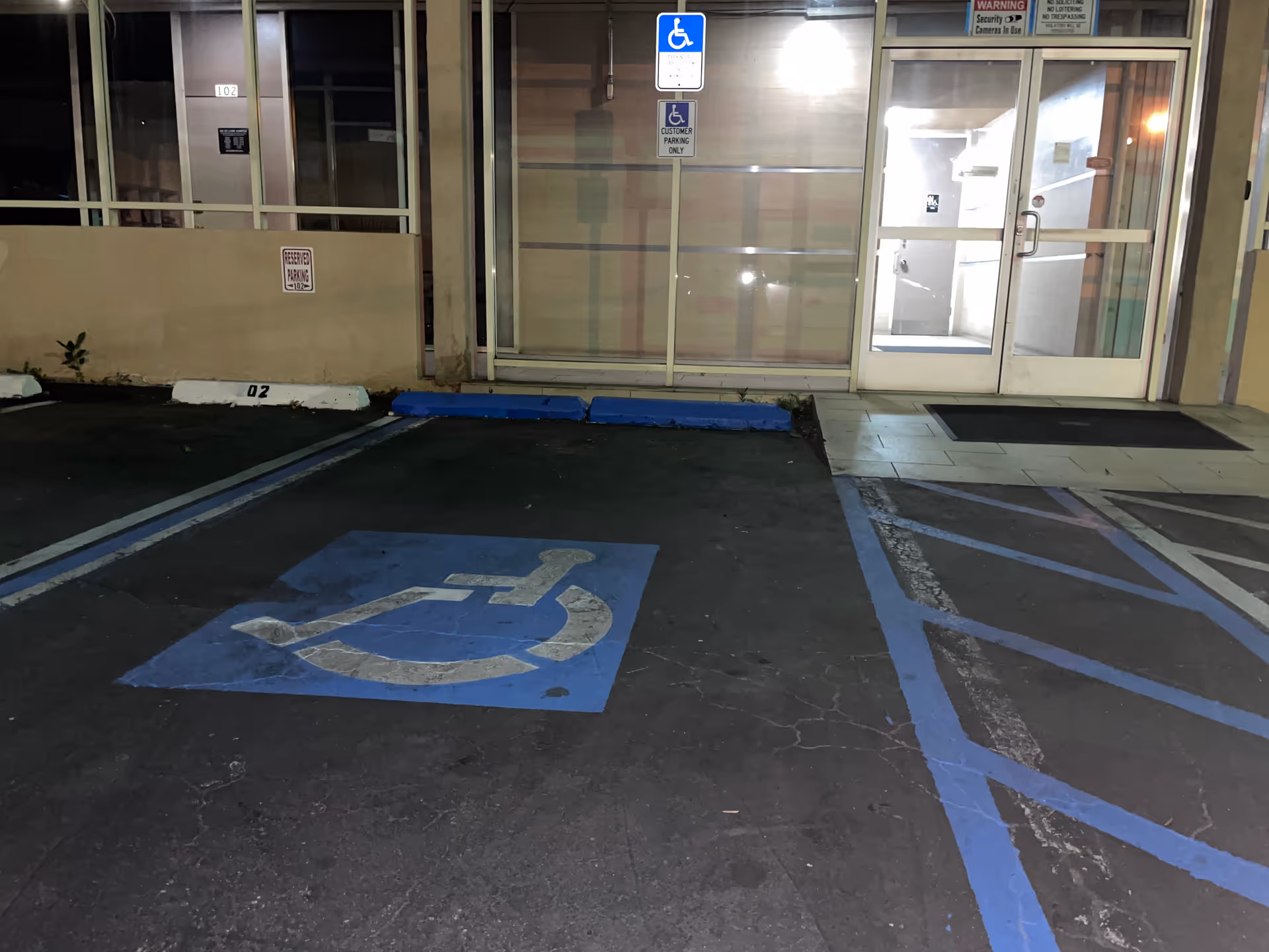 Night exterior of a facility entrance with handicap parking symbols and glass doors.