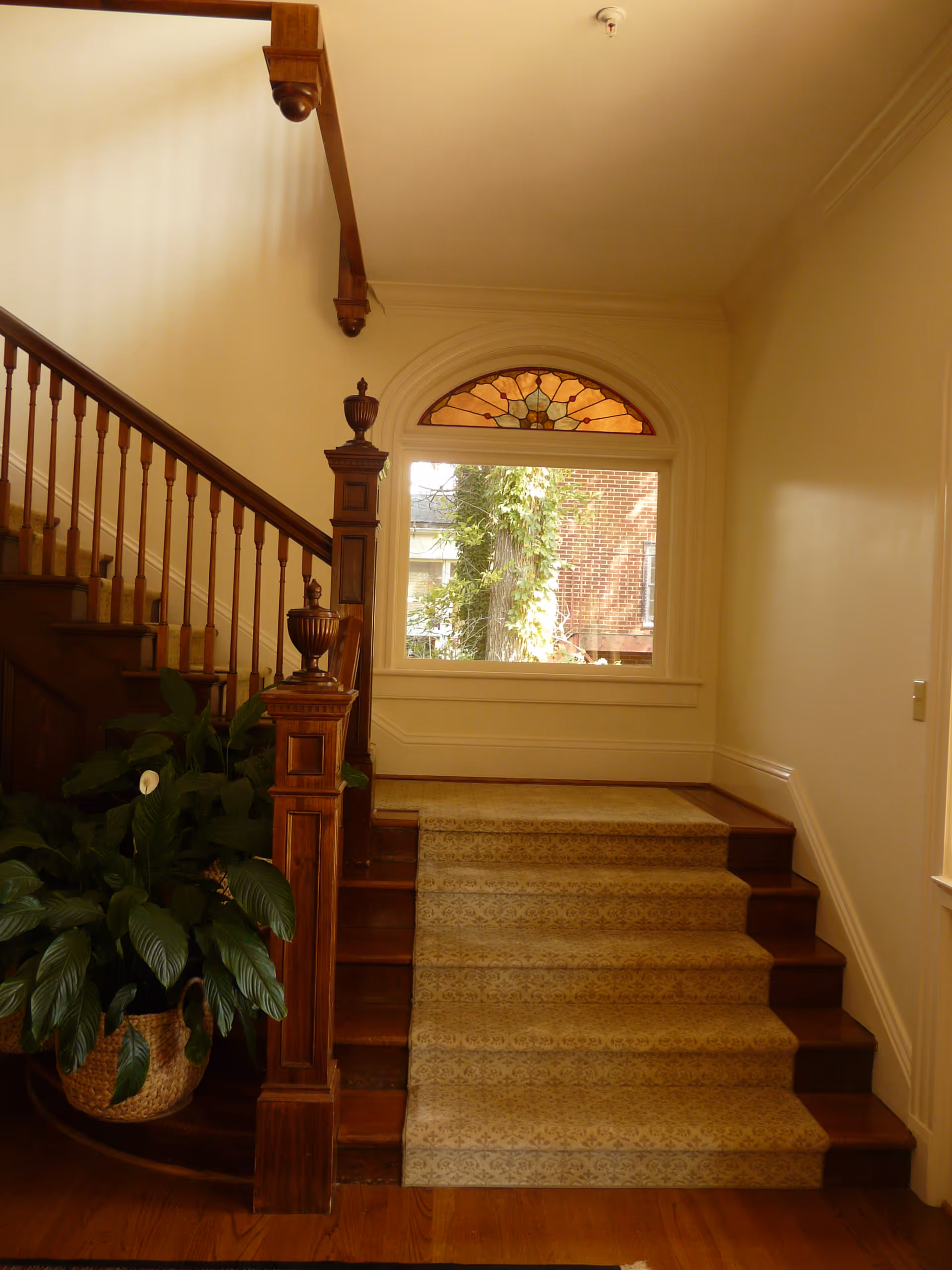 Interior staircase with carved wooden railing, carpeted steps, a potted plant, and a stained-glass window.