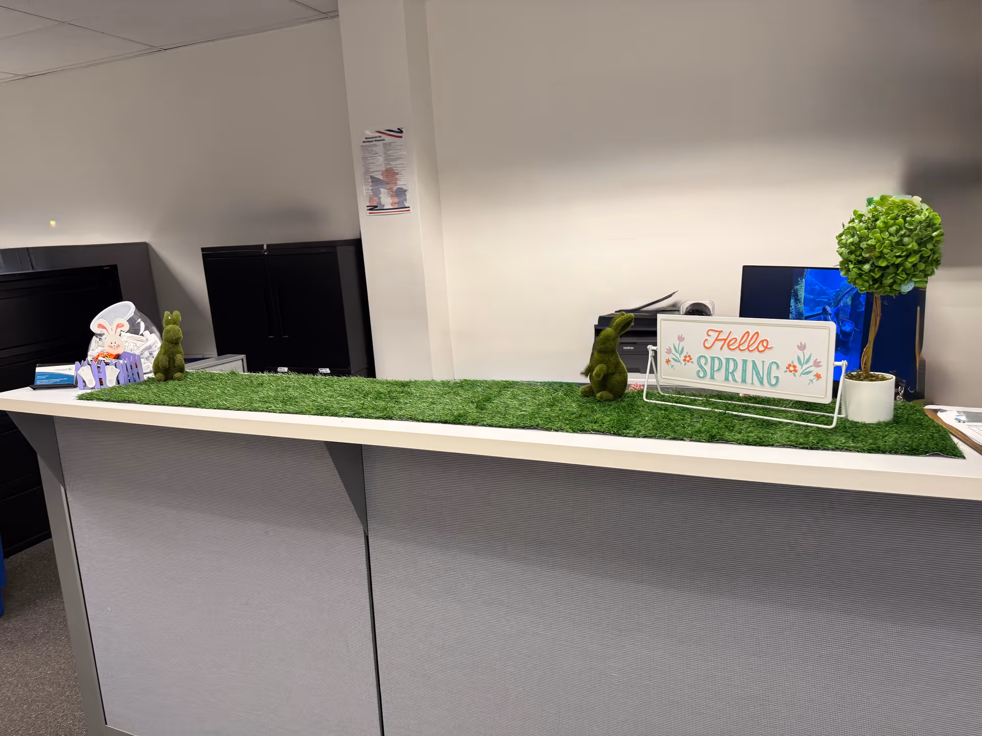 Reception desk with artificial grass surface and spring decor inside a facility.