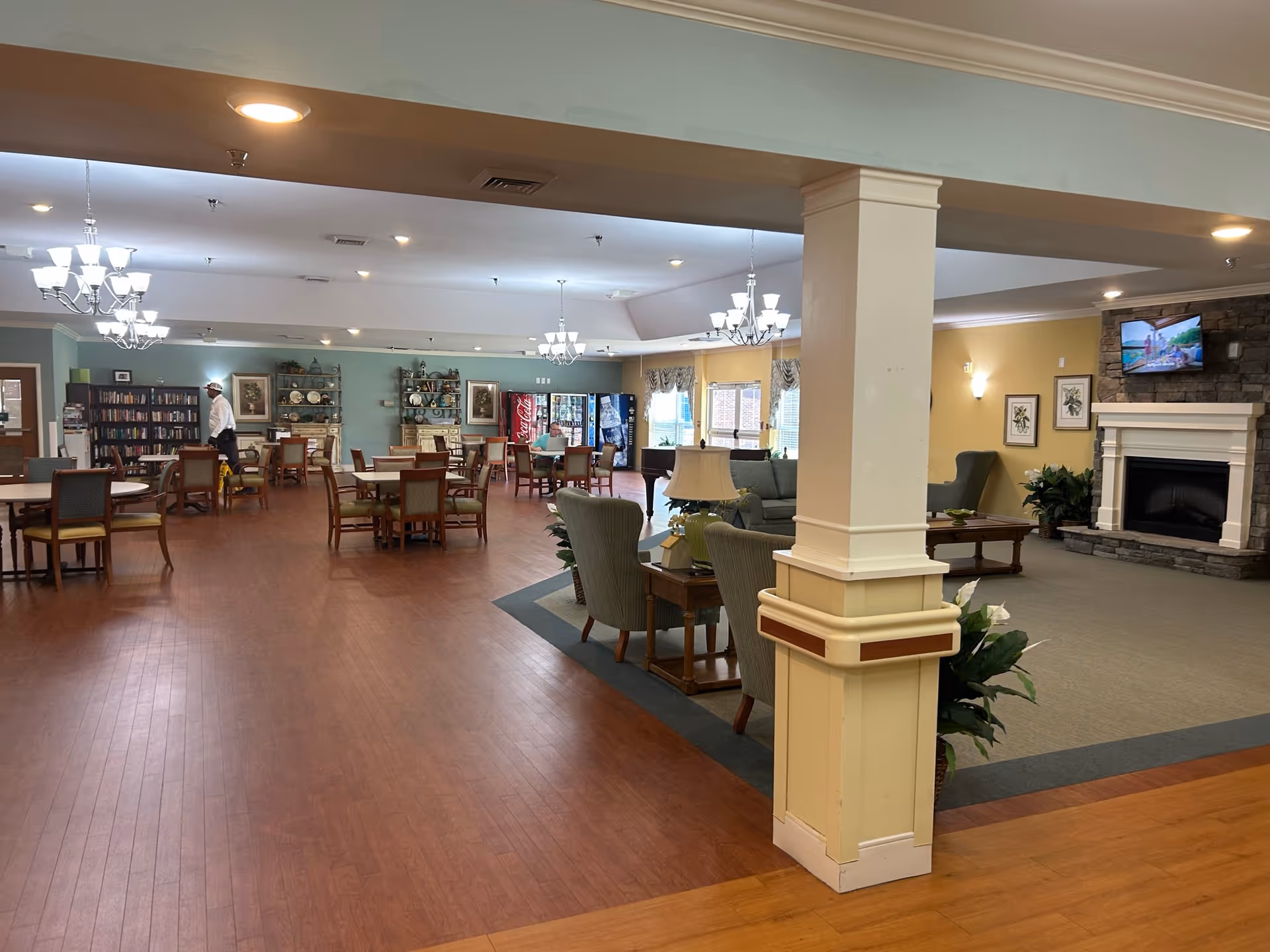 Spacious senior living common area with tables, chairs, a fireplace, and lounge seating.