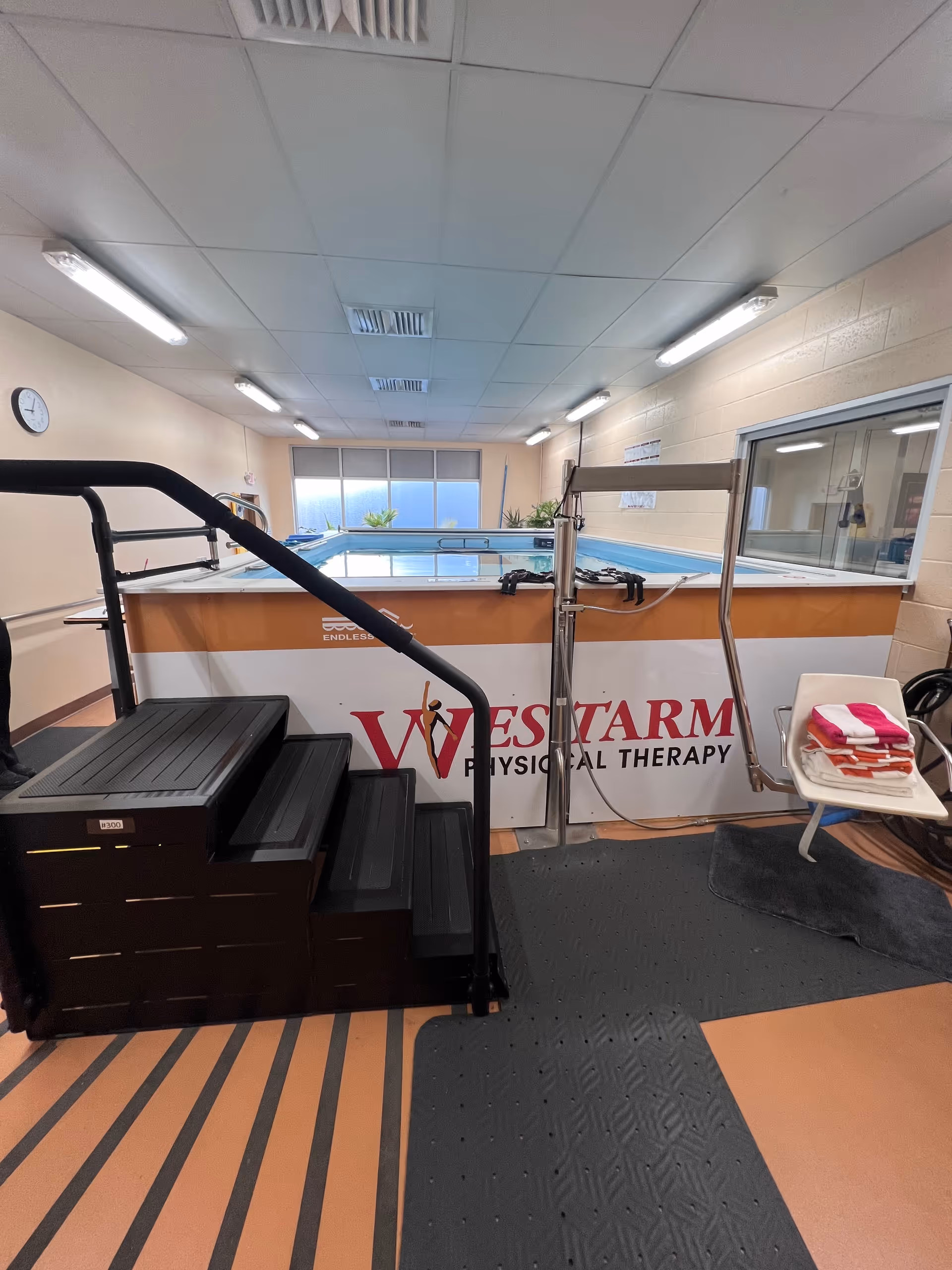 Indoor physical therapy pool area with steps, railing, and WESTARM Physical Therapy signage.