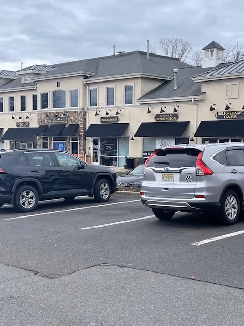 Exterior view of a strip mall with storefronts and parked cars.