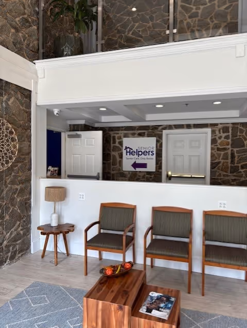 Stone-walled interior lobby with chairs, side table, lamp, and Senior Helpers sign.
