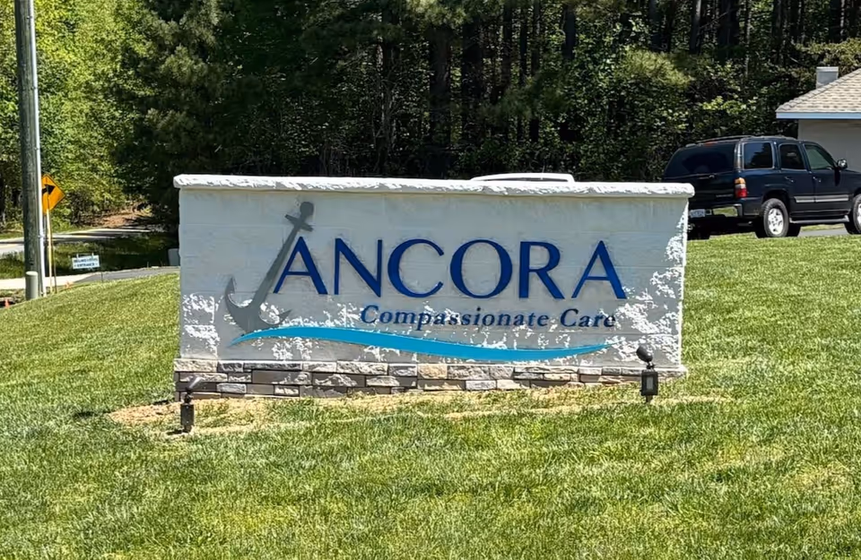 Stone sign reading Ancora Compassionate Care sits on a grassy lawn.