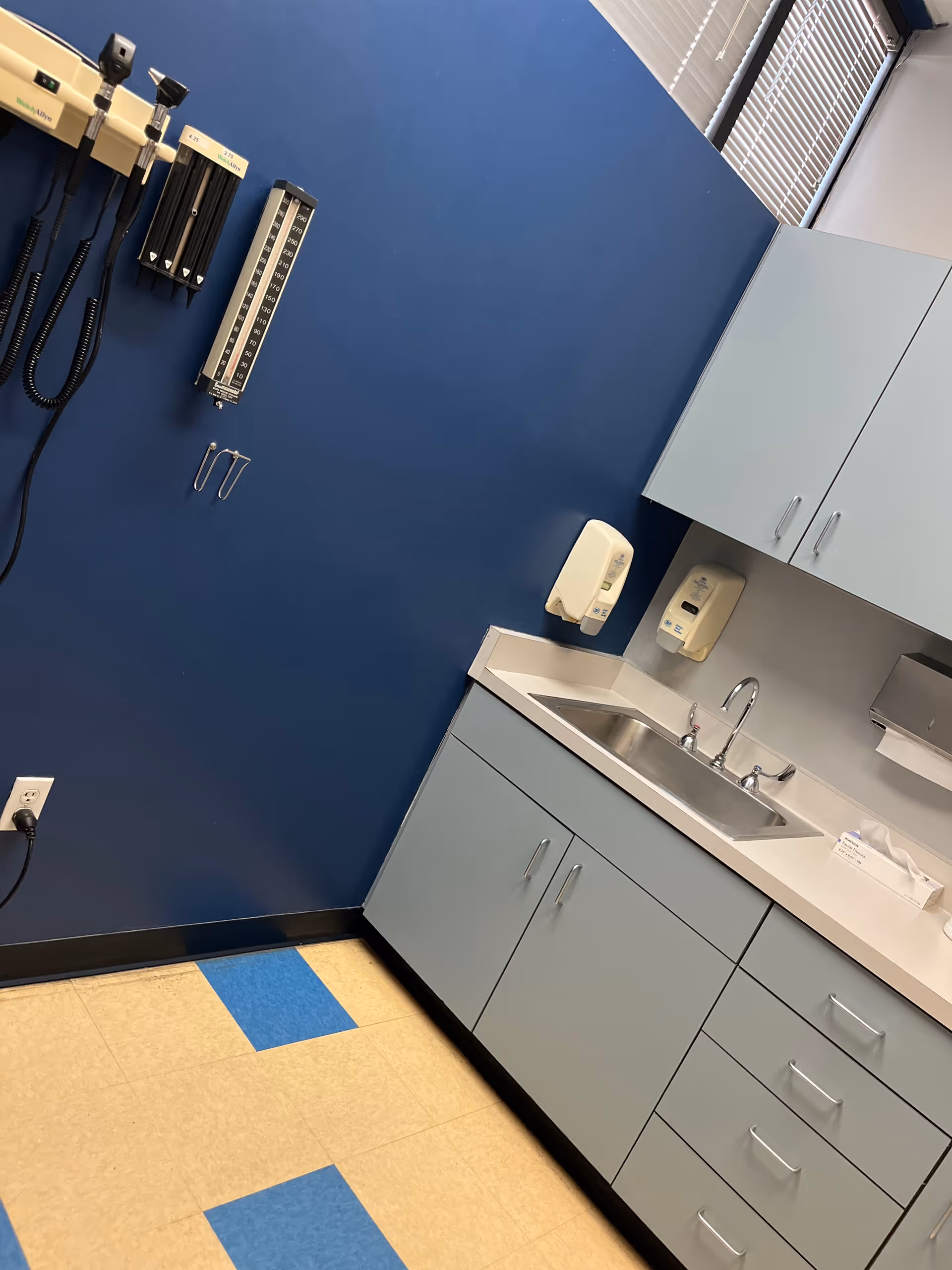 A blue clinic room with a sink, cabinets, and wall-mounted medical equipment.