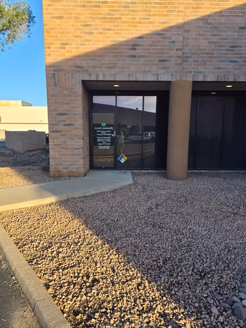 Exterior view of a brick facility entrance with glass doors and a gravel path.